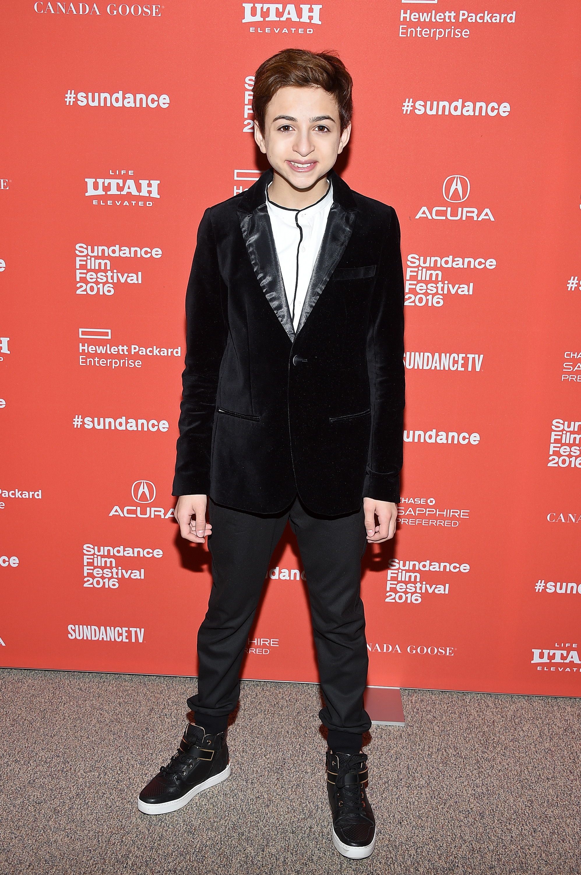 J.J. Totah lächelt den Fotografen bei der Premiere von „Other People“ während des Sundance Film Festivals in Park City, Utah, zu – er trägt einen schwarzen Samtblazer, ein weißes Hemd, eine schwarze Hose und High-Top-Sneaker. | Quelle: Getty Images