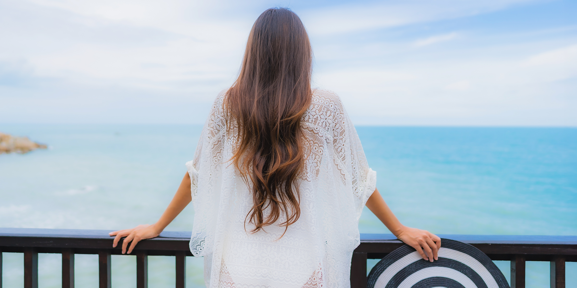 Eine Frau, die von einem Balkon aus auf das Meer schaut | Quelle: Shutterstock