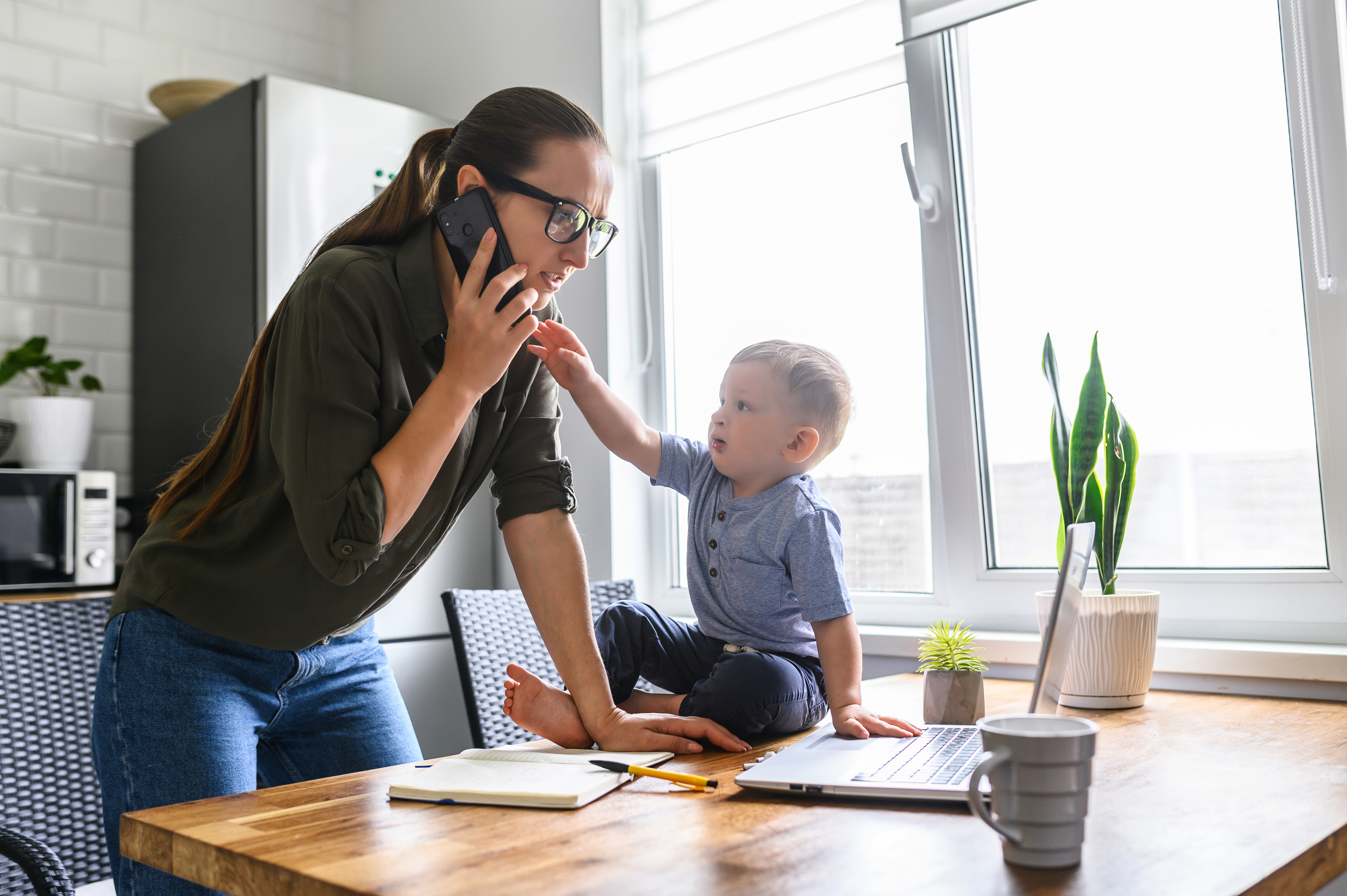 Junge Mutter am Telefon, während ihr kleiner Sohn danach greift | Quelle: Shutterstock