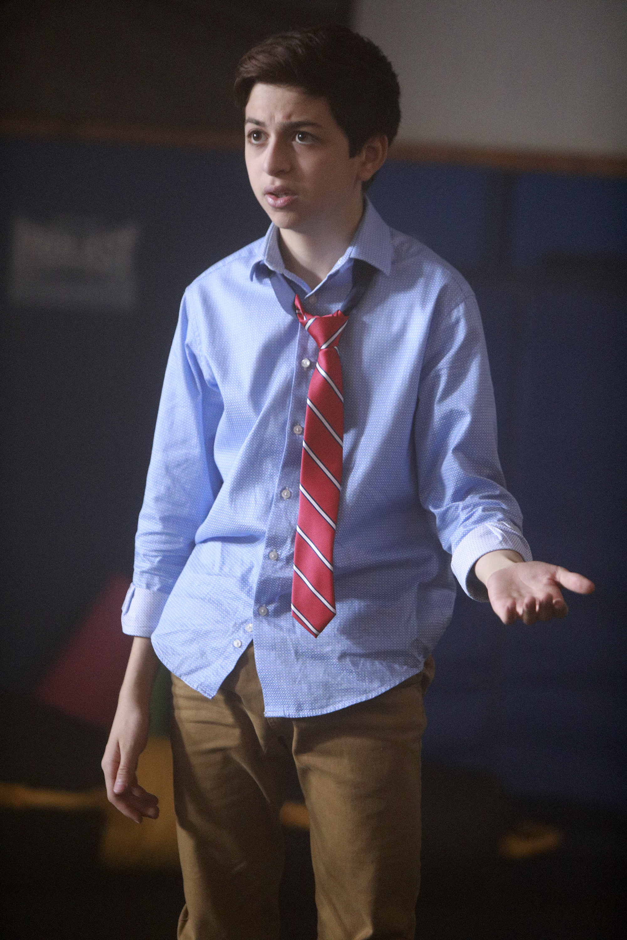 J.J. Totah spielt in einer Szene der Fernsehserie „Champions“ die Rolle des Michael und trägt dabei ein hellblaues Hemd mit Knöpfen, eine locker geknotete rot gestreifte Krawatte und eine braune Hose. | Quelle: Getty Images