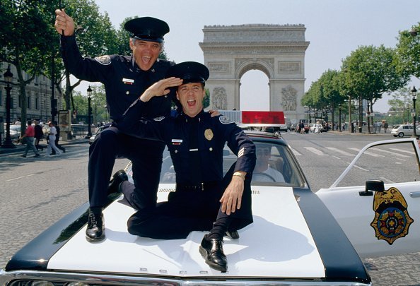 G.W. Bailey und Lance Kinsey fahren in einem Polizeiauto die Champs-Elysees hinunter | Quelle: Getty Images