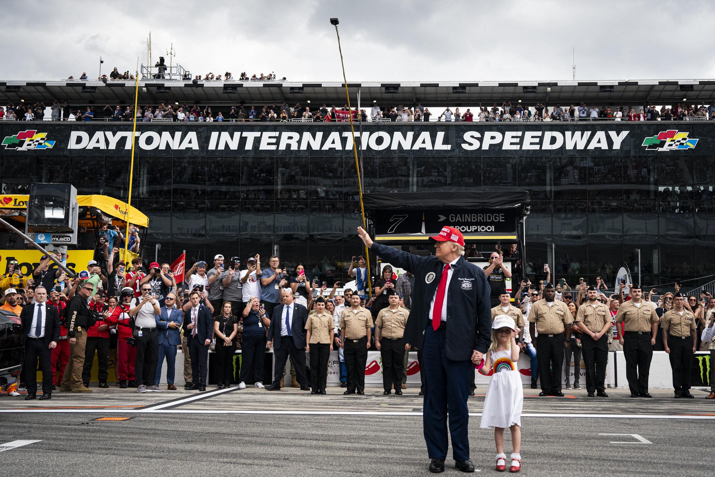 Präsident Donald Trump, begleitet von seiner Enkelin Carolina Trump, begrüßt die Anwesenden vor der Fahrt in der Präsidentenlimousine vor dem Start des Daytona 500 Nascar-Rennens auf dem Daytona International Speedway in Daytona Beach, Florida, am 16. Februar 2025 | Quelle: Getty Images