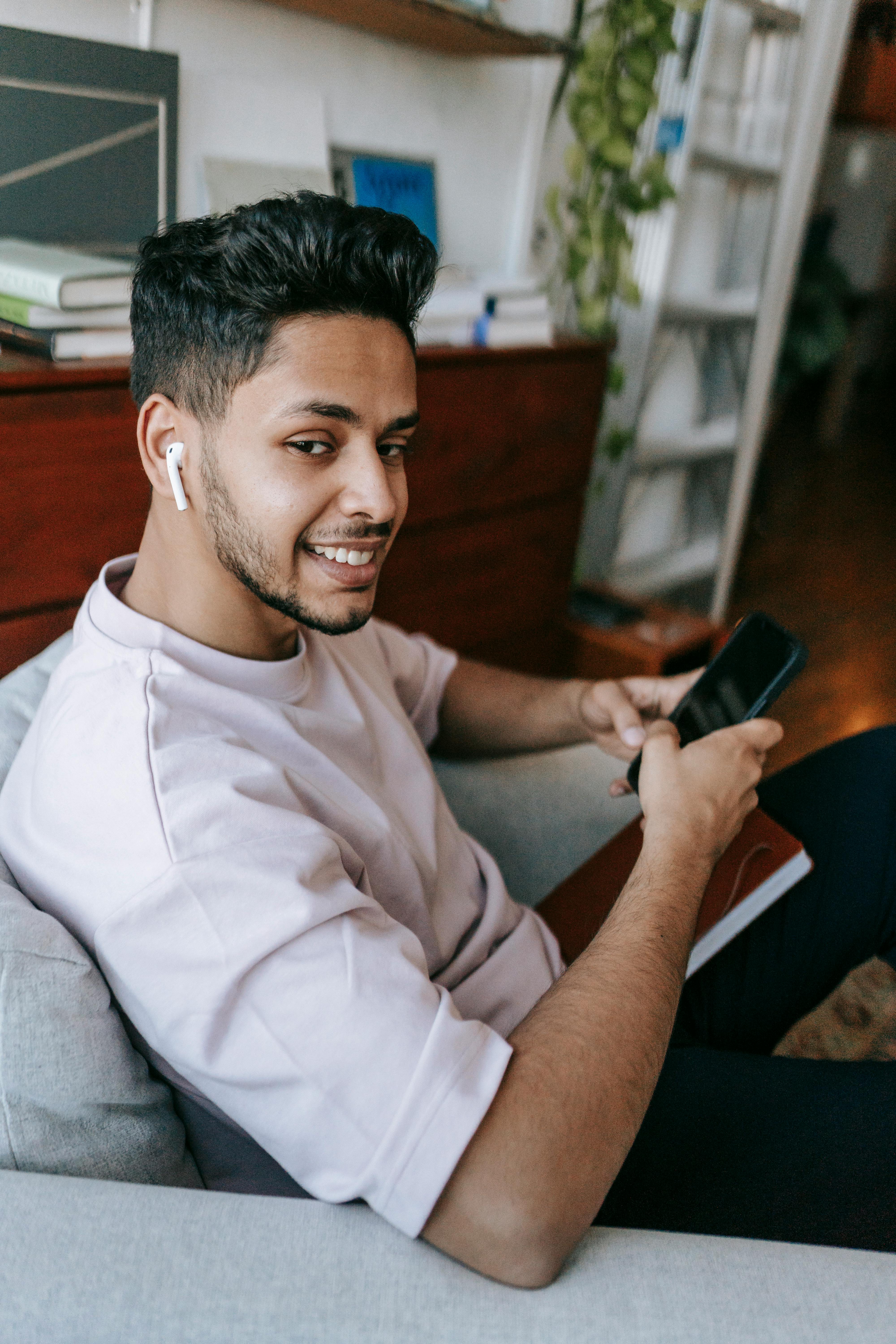 Ein glücklicher Mann, der sein Telefon und seine Ohrstöpsel benutzt | Quelle: Pexels