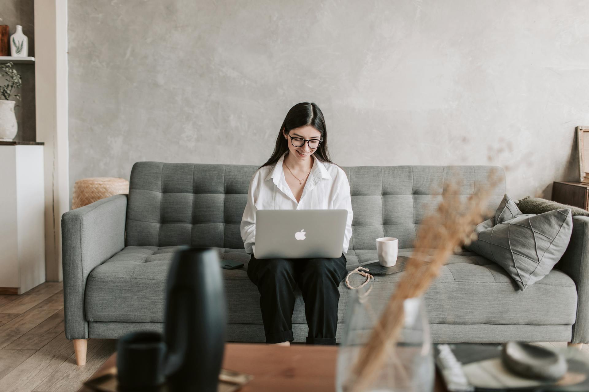 Eine Frau auf einer Couch, die Kaffee trinkt und einen Laptop benutzt | Quelle: Pexels