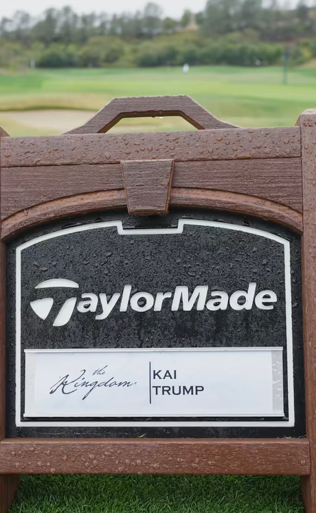 Ein TaylorMade-Schild mit Kai Trumps Namen steht auf einem verschwommenen Fairway, das mit Regentropfen auf seinem Holzrahmen übersät ist | Quelle: Tiktok/thekaitrumpgolfer