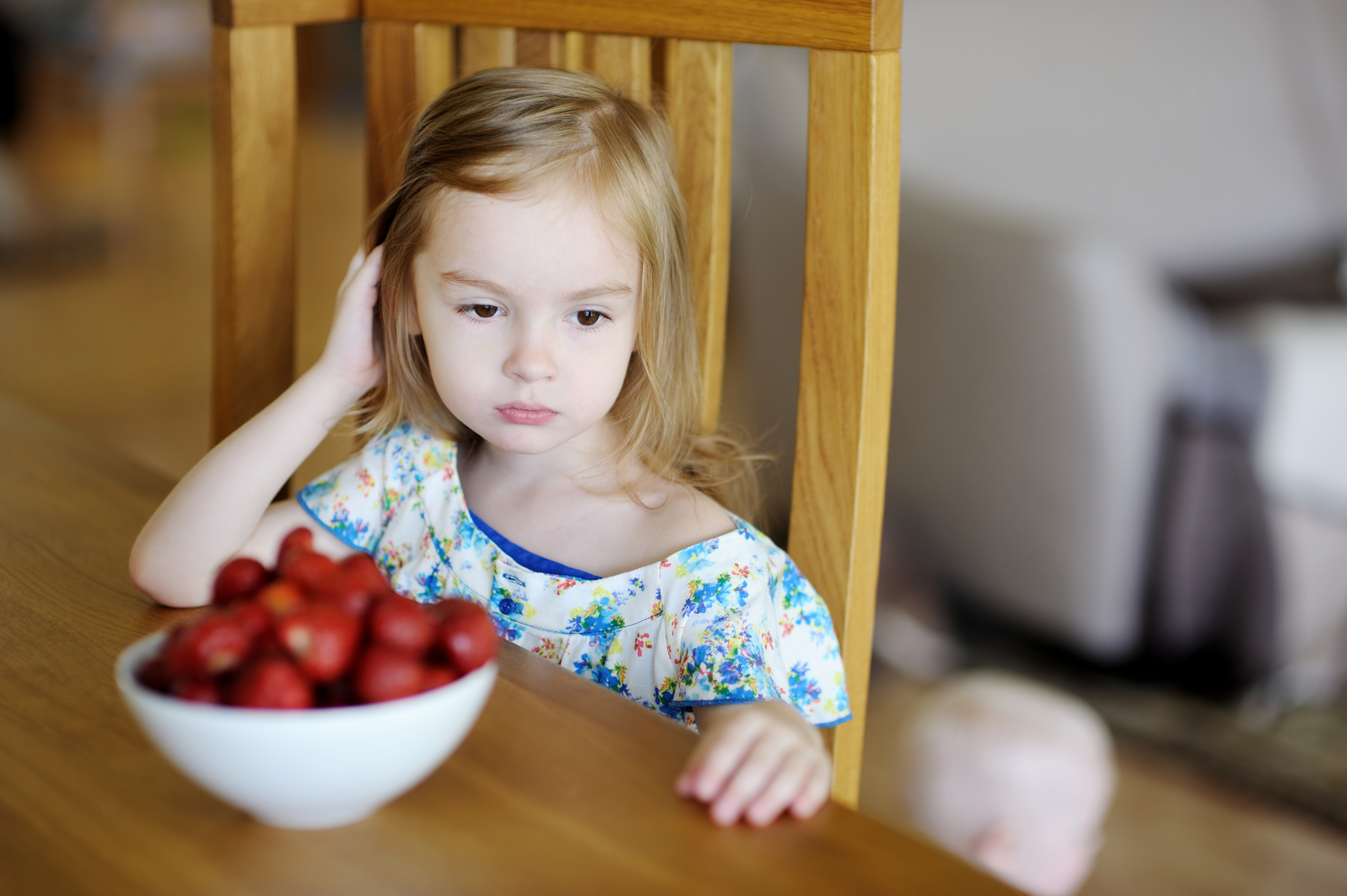 Kleines Mädchen mit traurigem Blick und einer Schale Erdbeeren vor sich am Esstisch | Quelle: Shutterstock