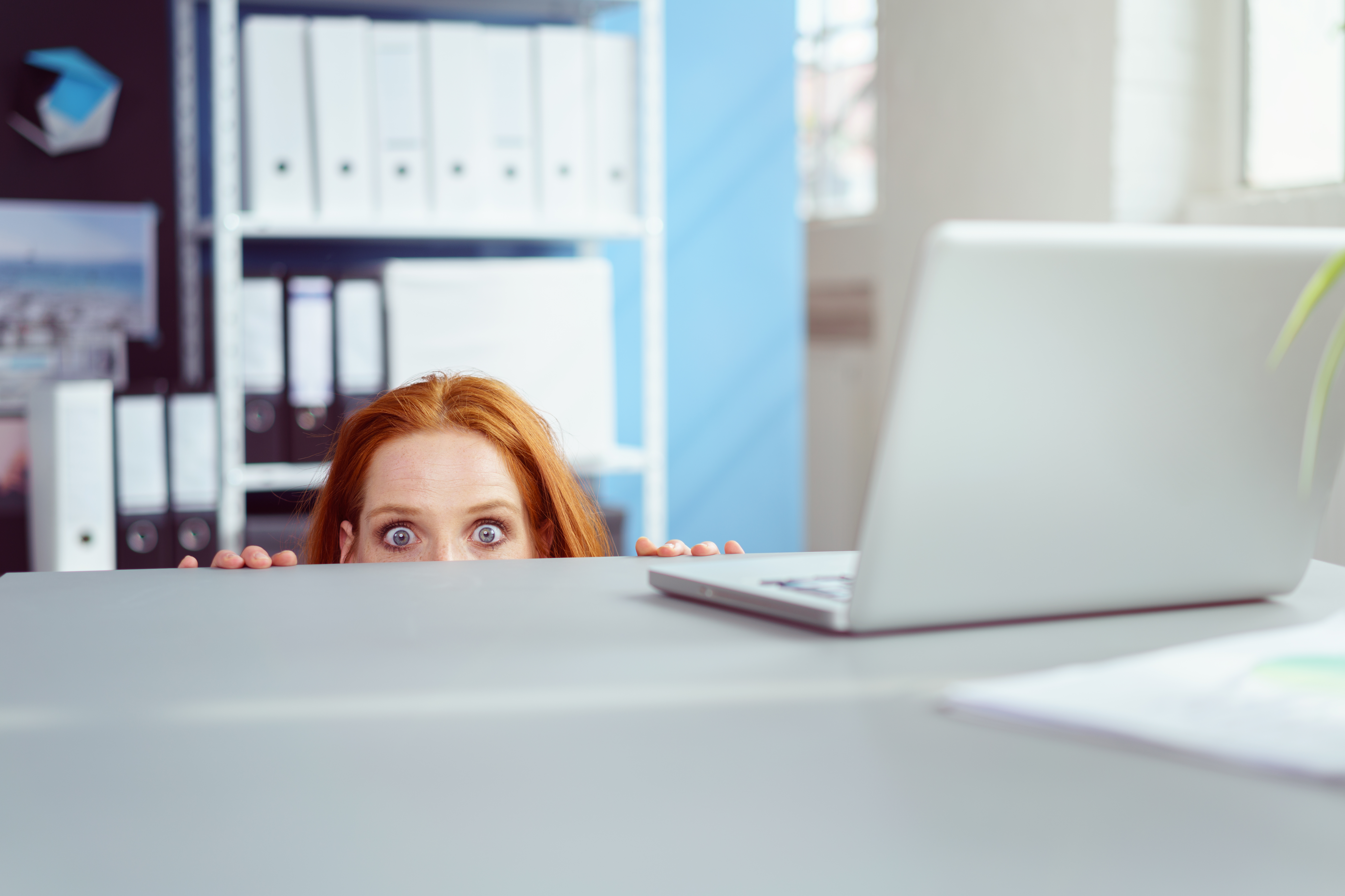 Eine Frau versteckt sich unter einem Schreibtisch | Quelle: Shutterstock