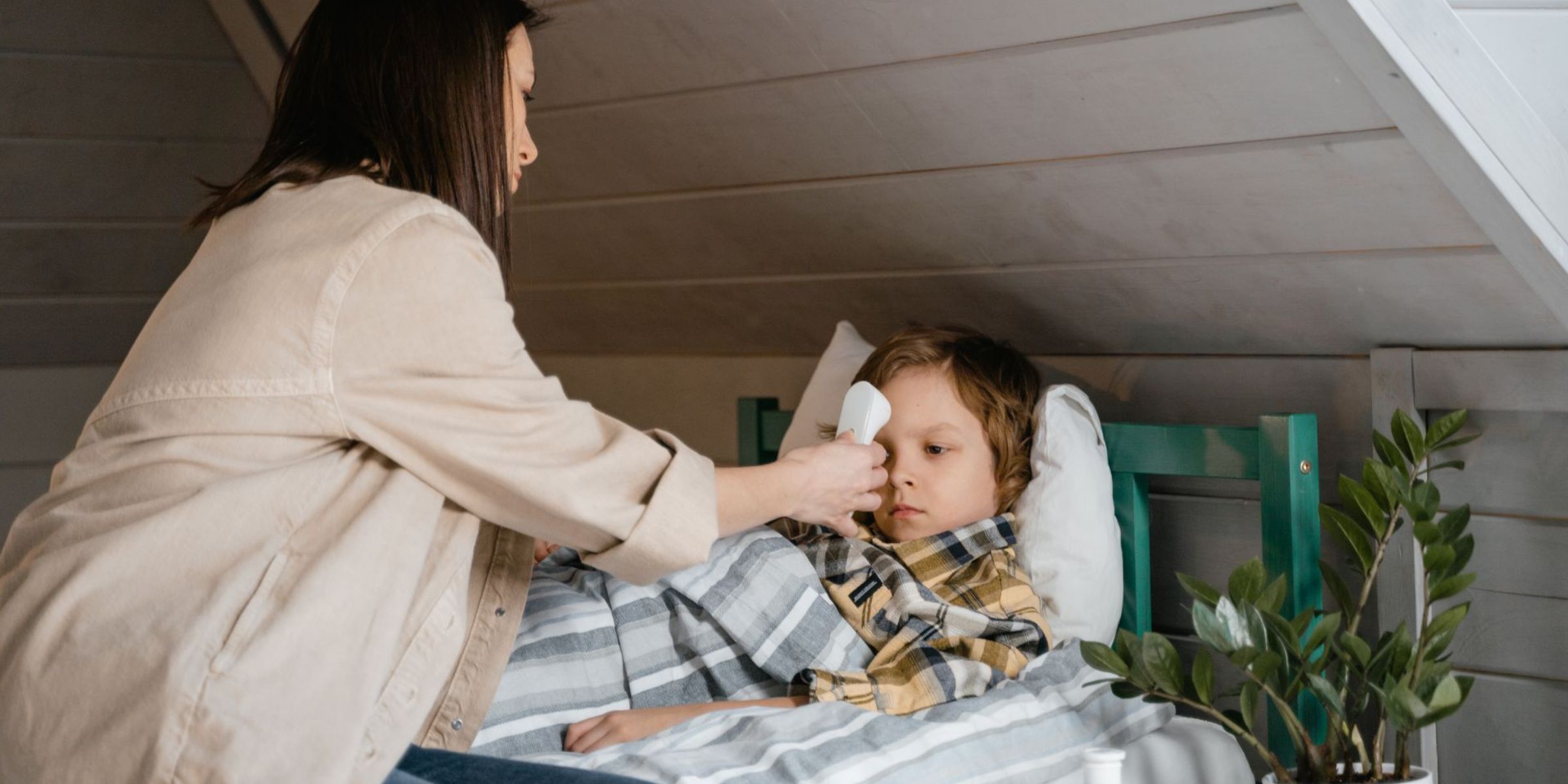 Eine Mutter misst die Temperatur ihres kranken Kindes, während es im Bett liegt | Quelle: Pexels