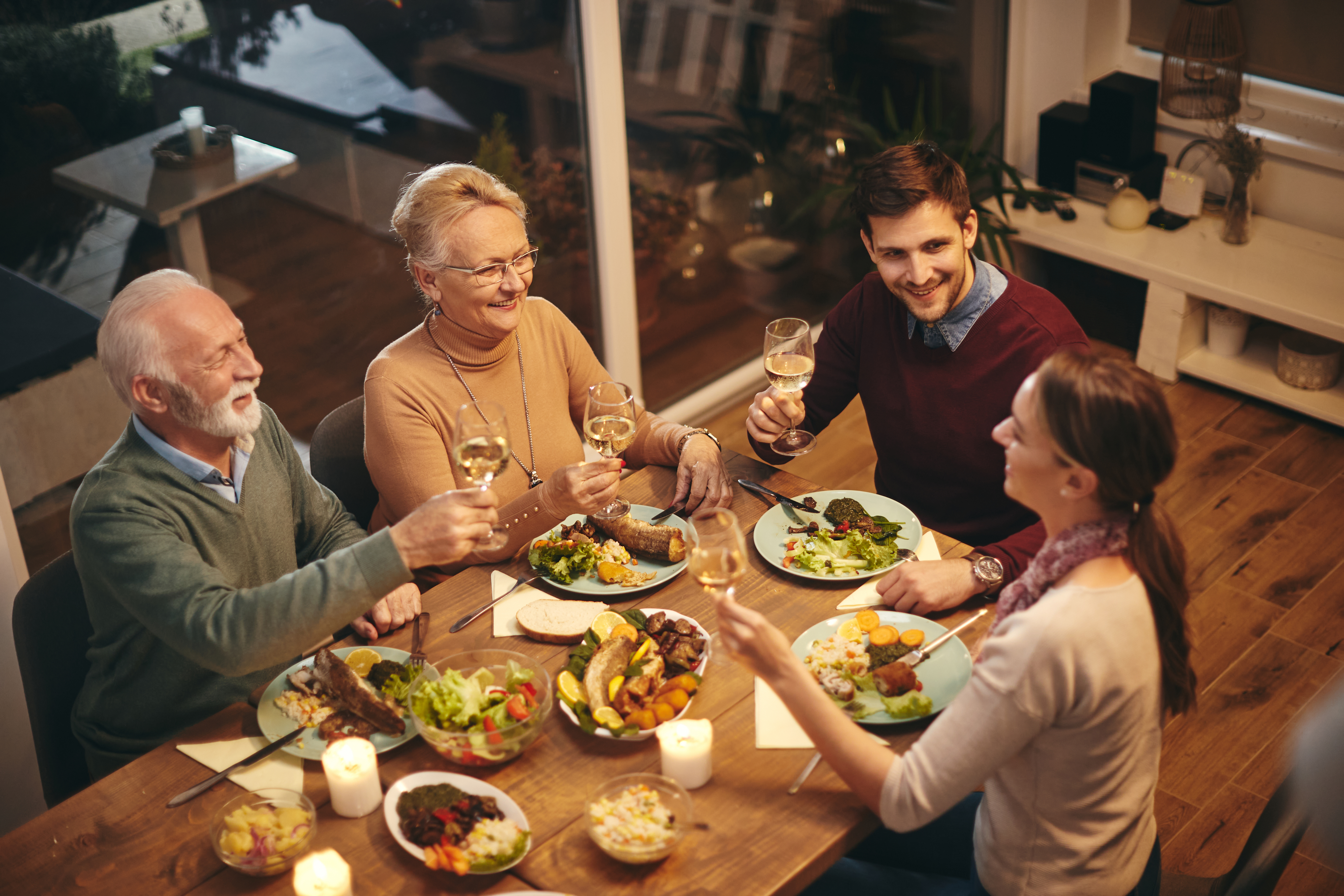 Eine glückliche ältere Frau stößt mit ihrer Familie an, während sie eine Mahlzeit am Esstisch einnimmt | Quelle: Shutterstock