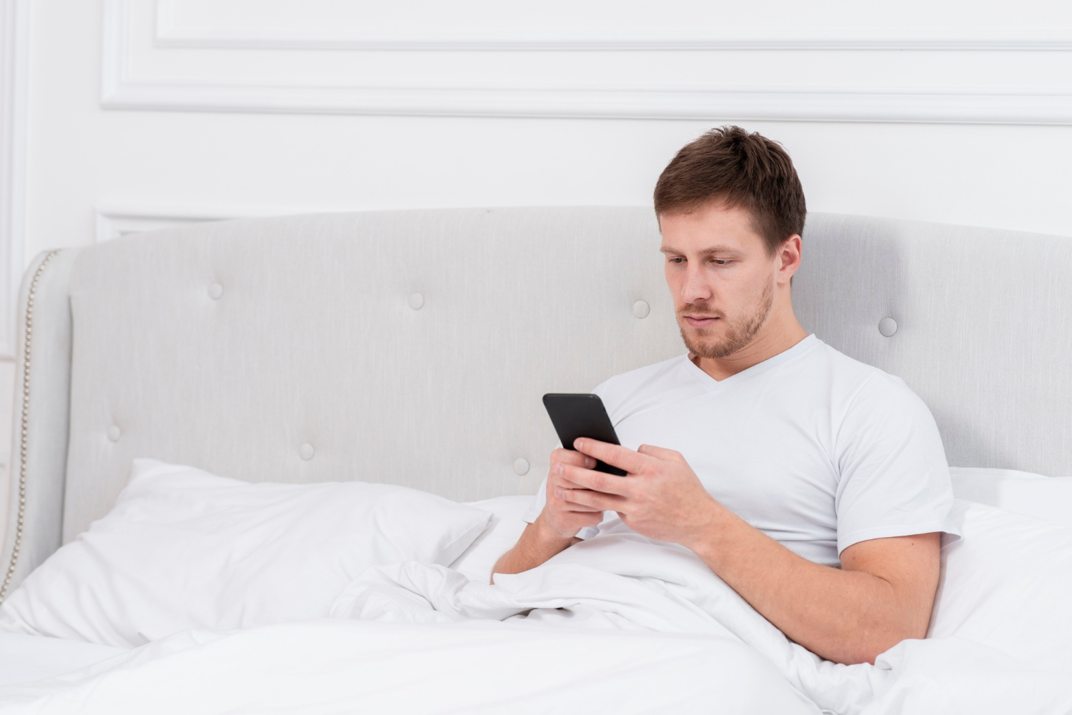 Ein Mann sitzt auf seinem Bett und starrt auf sein Telefon | Quelle: Freepik