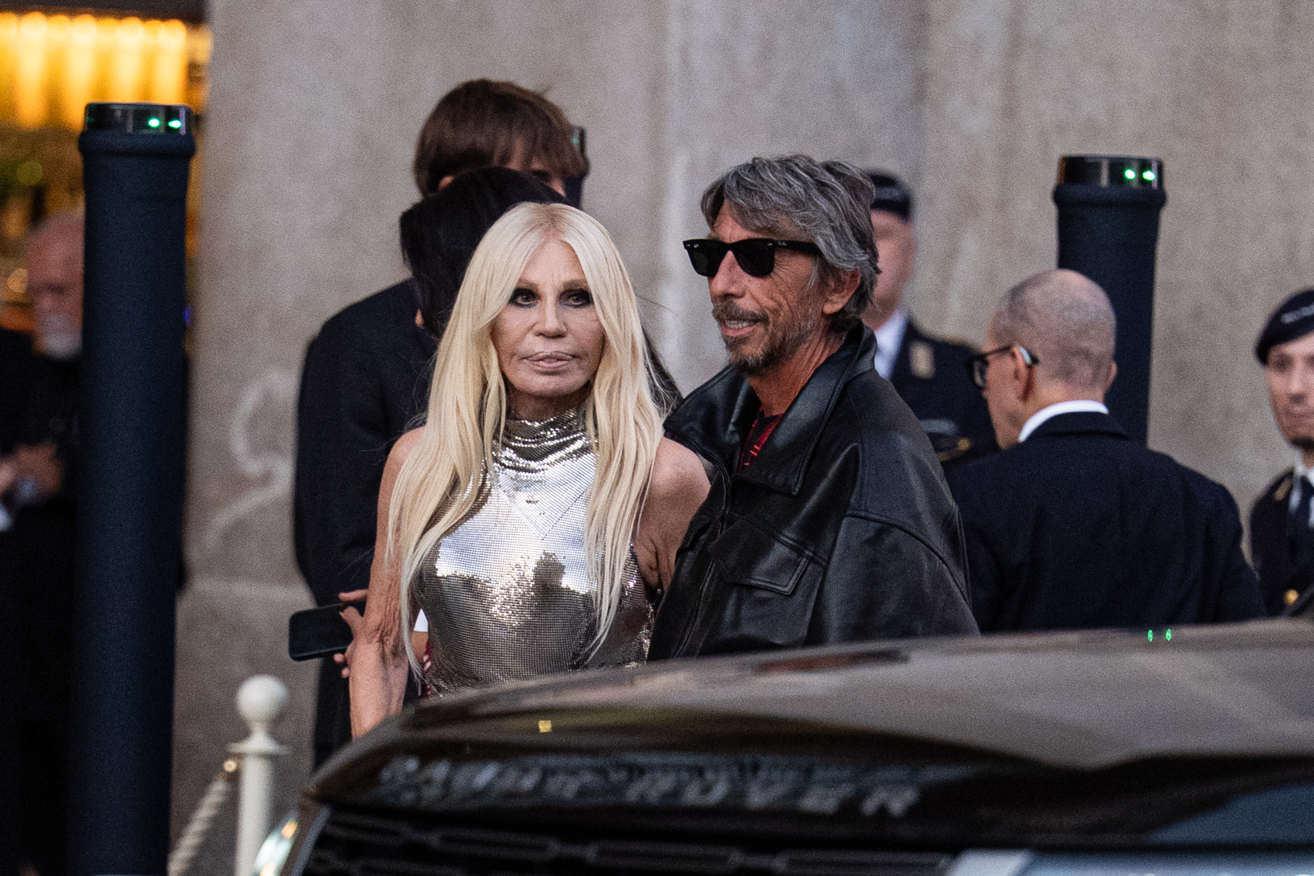 Versace erscheint an der Seite von Pierpaolo Piccioli; die Nahaufnahme hebt ihr silbern schimmerndes Oberteil und ihr langes platinblondes Haar hervor. | Quelle: Getty Images