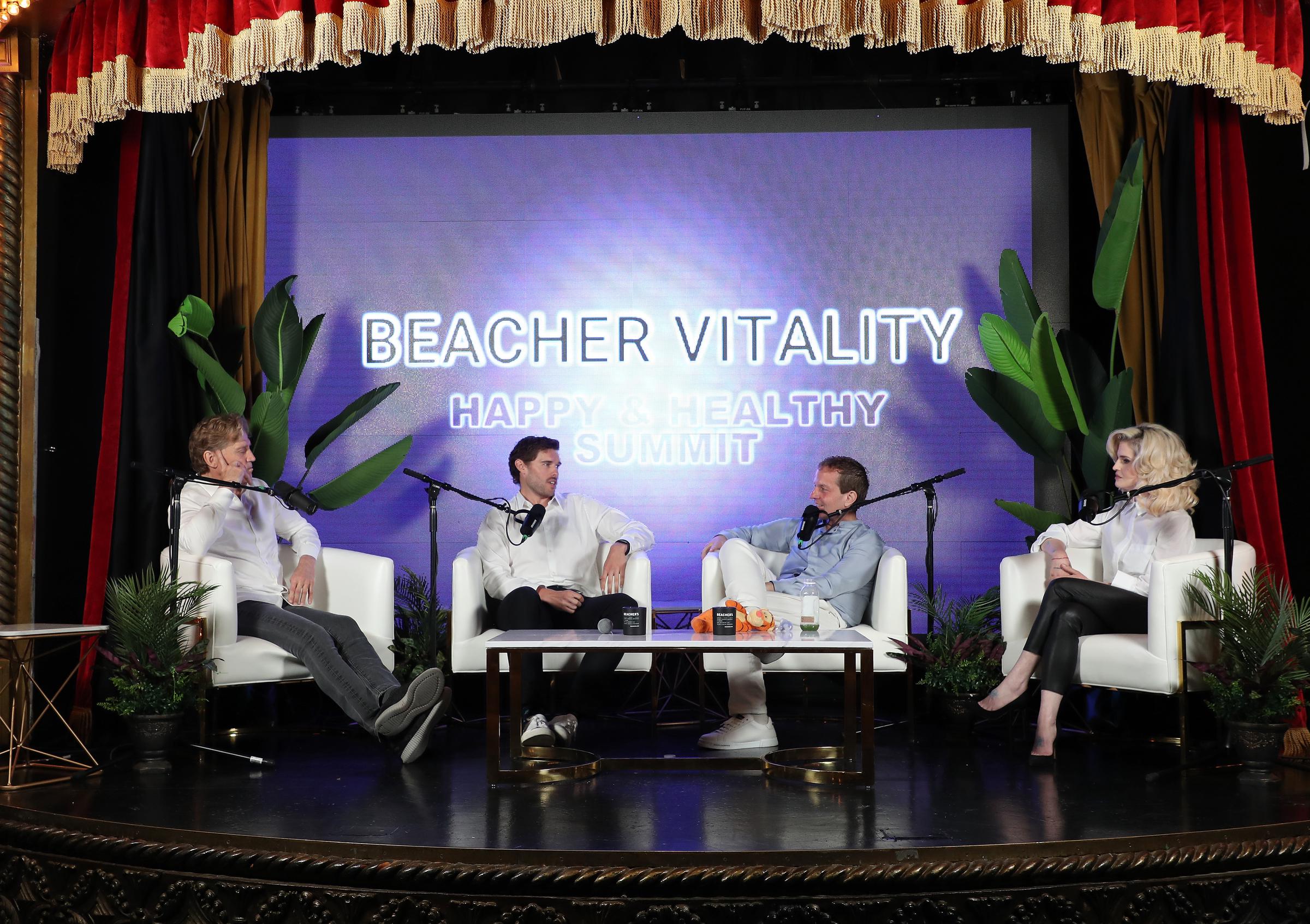 Christopher Schwarzenegger ist auf dem Beacher Vitality Happy & Healthy Summit am 10. Mai 2025 zu sehen. Er sitzt neben Dr. Robert Huizenga, Jeff Beacher und Kelly Osbourne und unterhält sich in einem weißen Hemd und einer schwarzen Hose über Gesundheit und Veränderung.