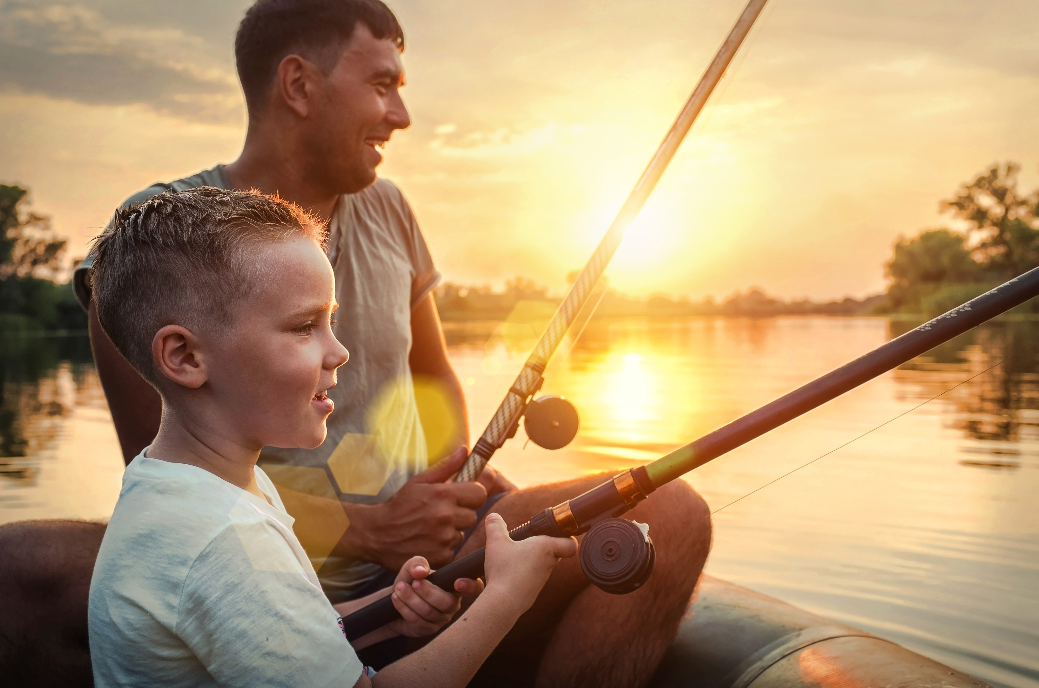 Vater und Sohn angeln gemeinsam von einem Boot aus bei Sonnenuntergang | Quelle: Shutterstock