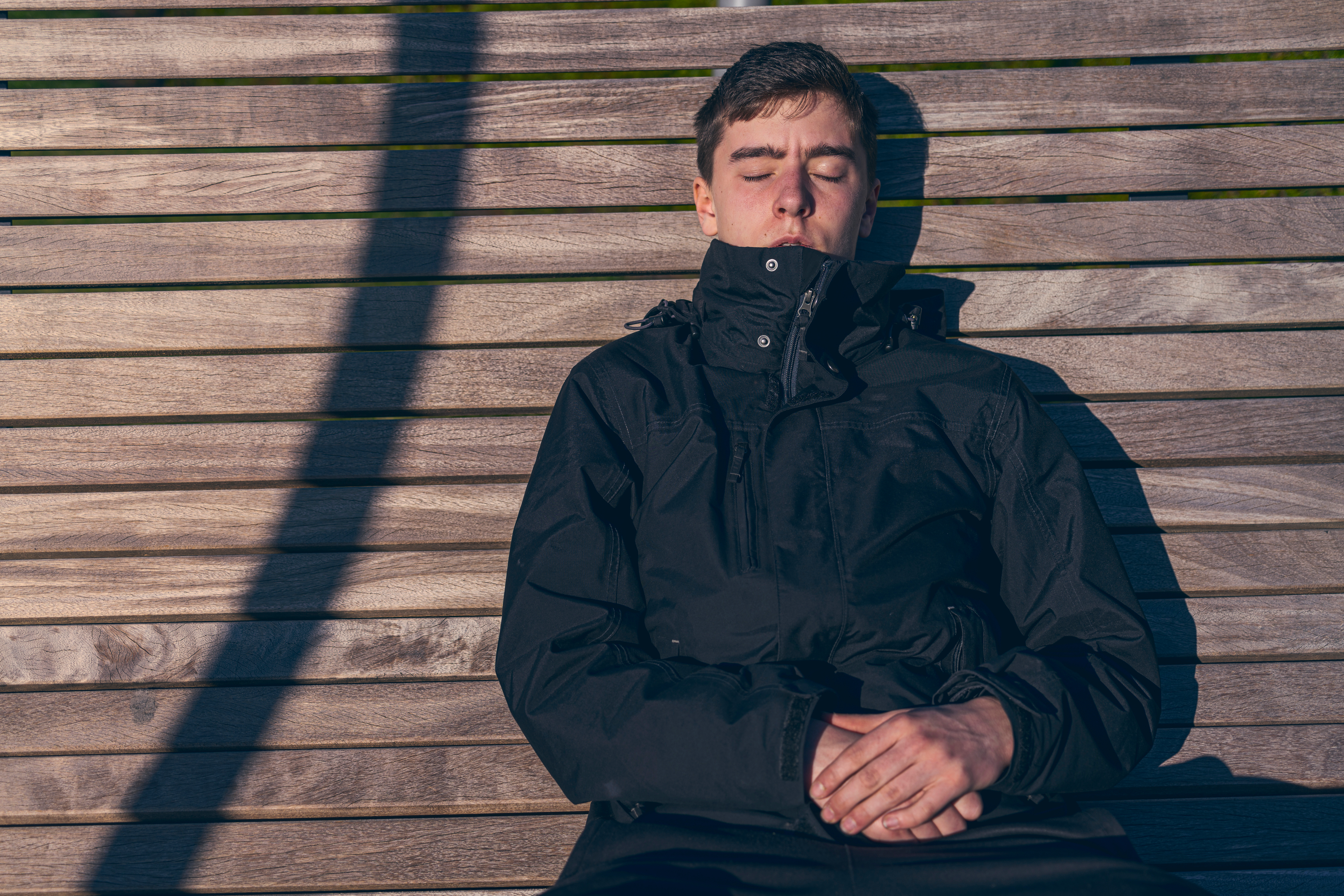 Junger Mann sitzt mit geschlossenen Augen auf einer Bank in der Sonne | Quelle: Shutterstock