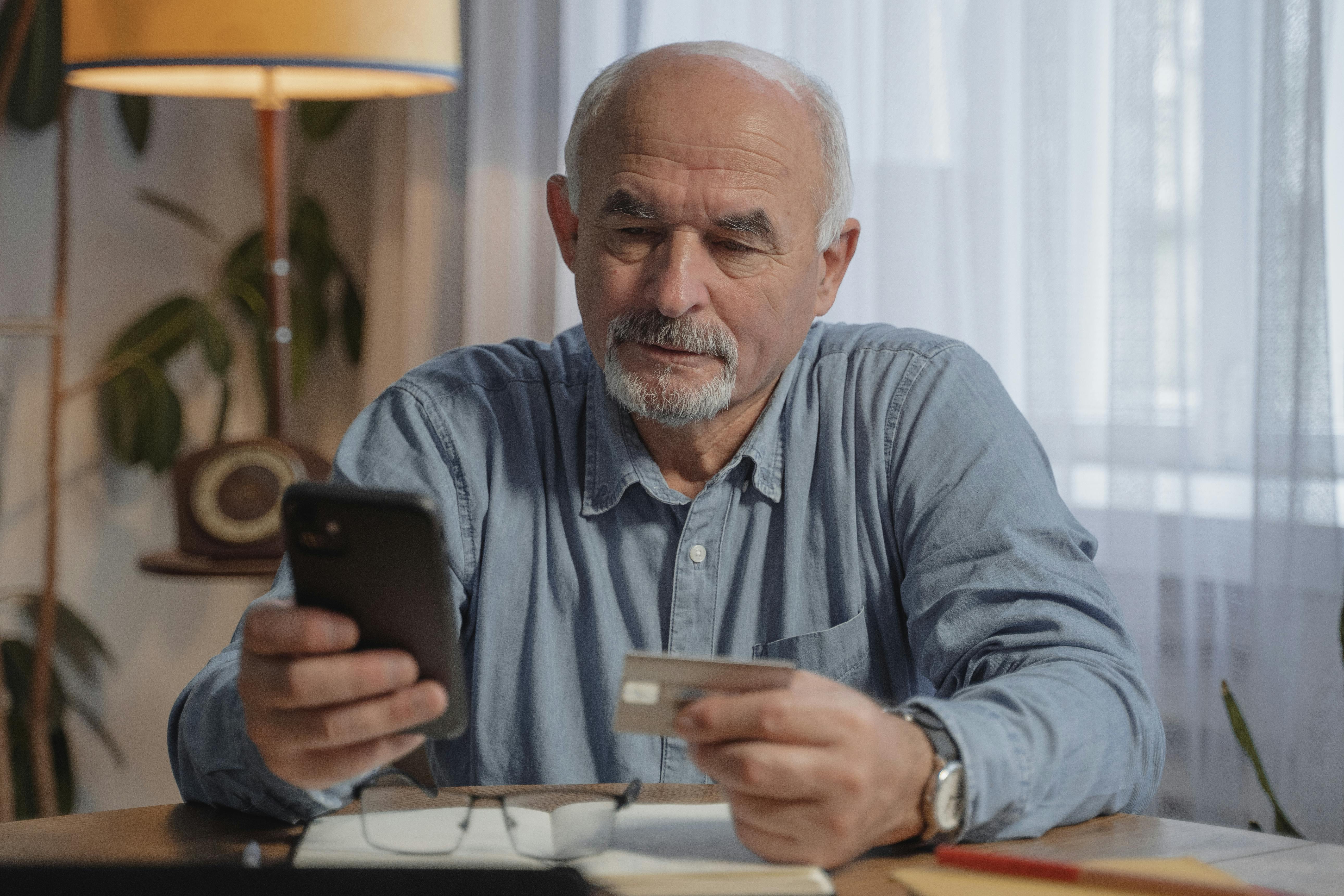 Ein älterer Mann hält sein Telefon in der einen und eine Bankkarte in der anderen Hand | Quelle: Pexels