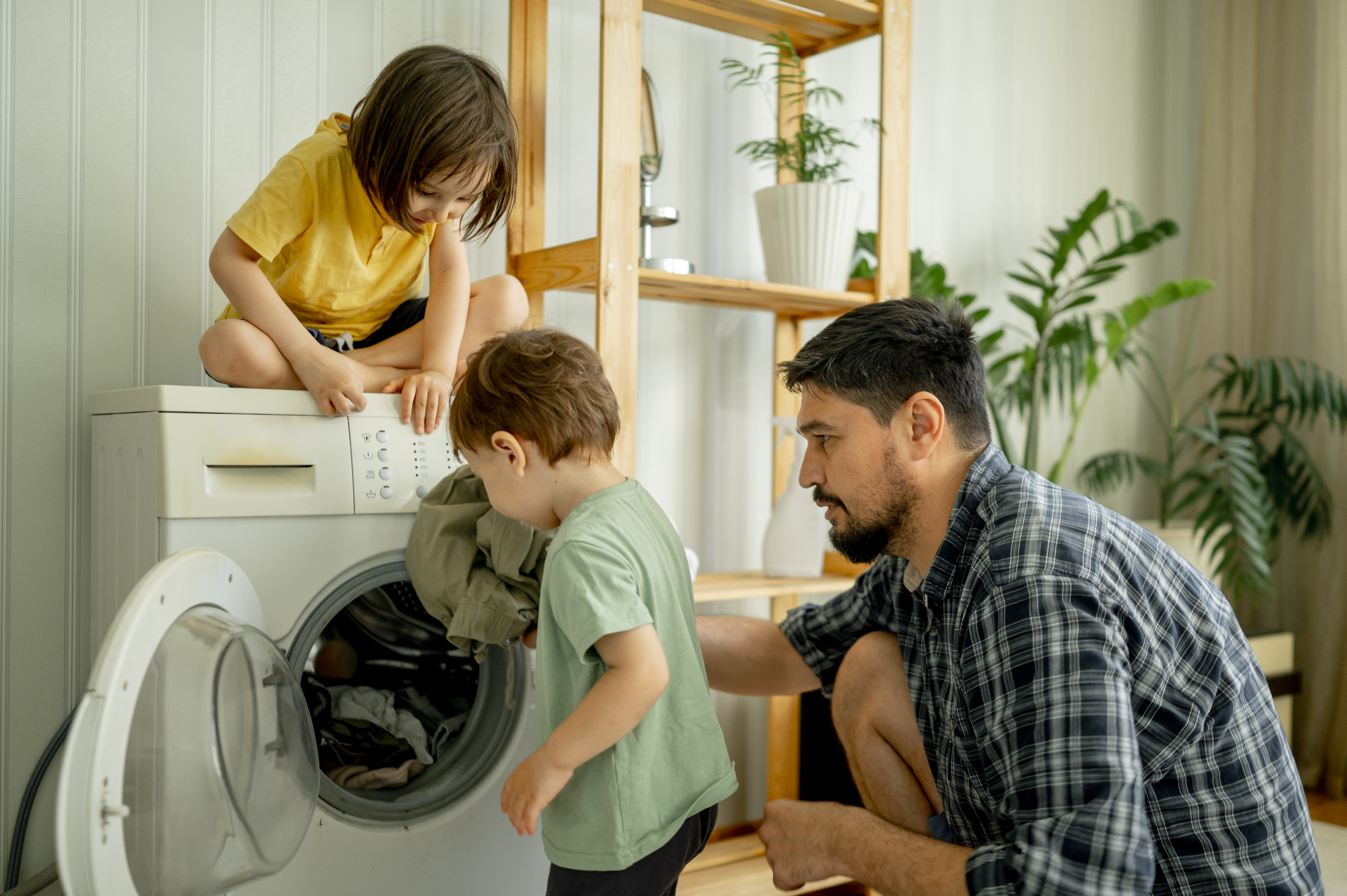 Vater mit Kindern hilft beim Waschen der Wäsche in der Maschine zu Hause | Quelle: Getty Images