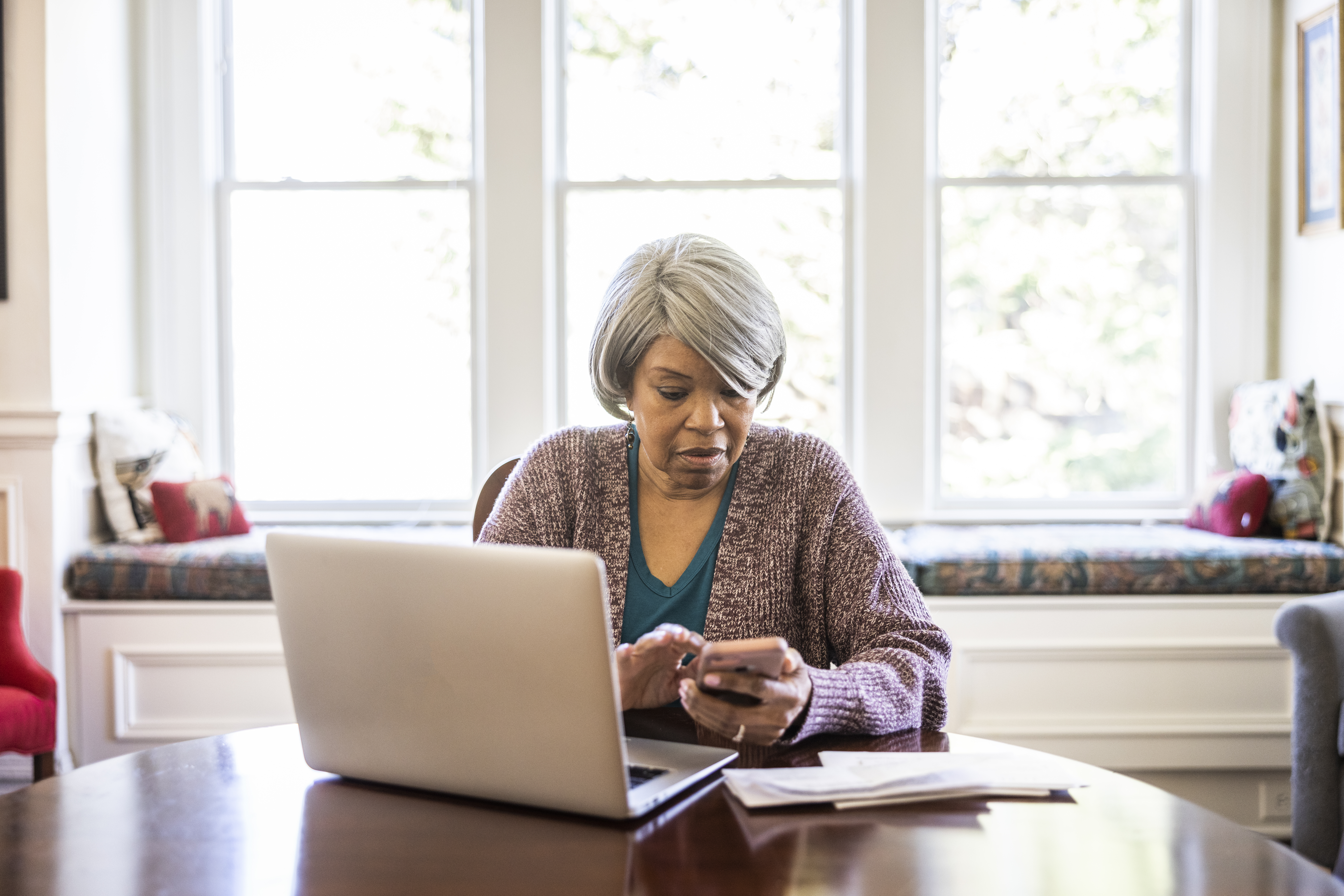 Ältere Frau bezahlt Rechnungen mit Laptop und Smartphone zu Hause | Quelle: Getty Images
