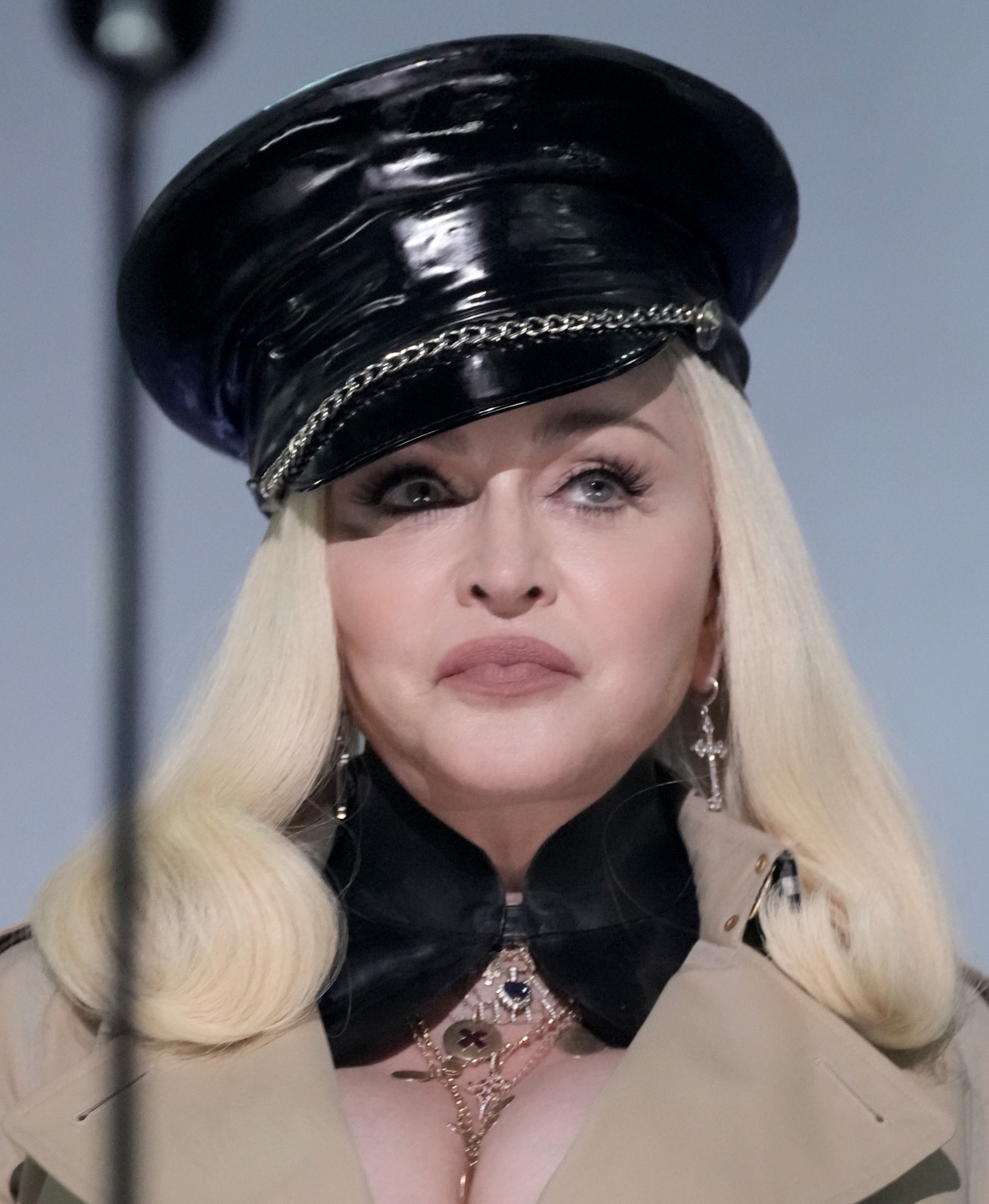 Madonna trägt eine glänzende schwarze Mütze mit Kettenverzierungen, hat langes platinblondes Haar, trägt baumelnde Ohrringe und mehrere Schichten Kleidung und Schmuck. | Quelle: Chat GPT