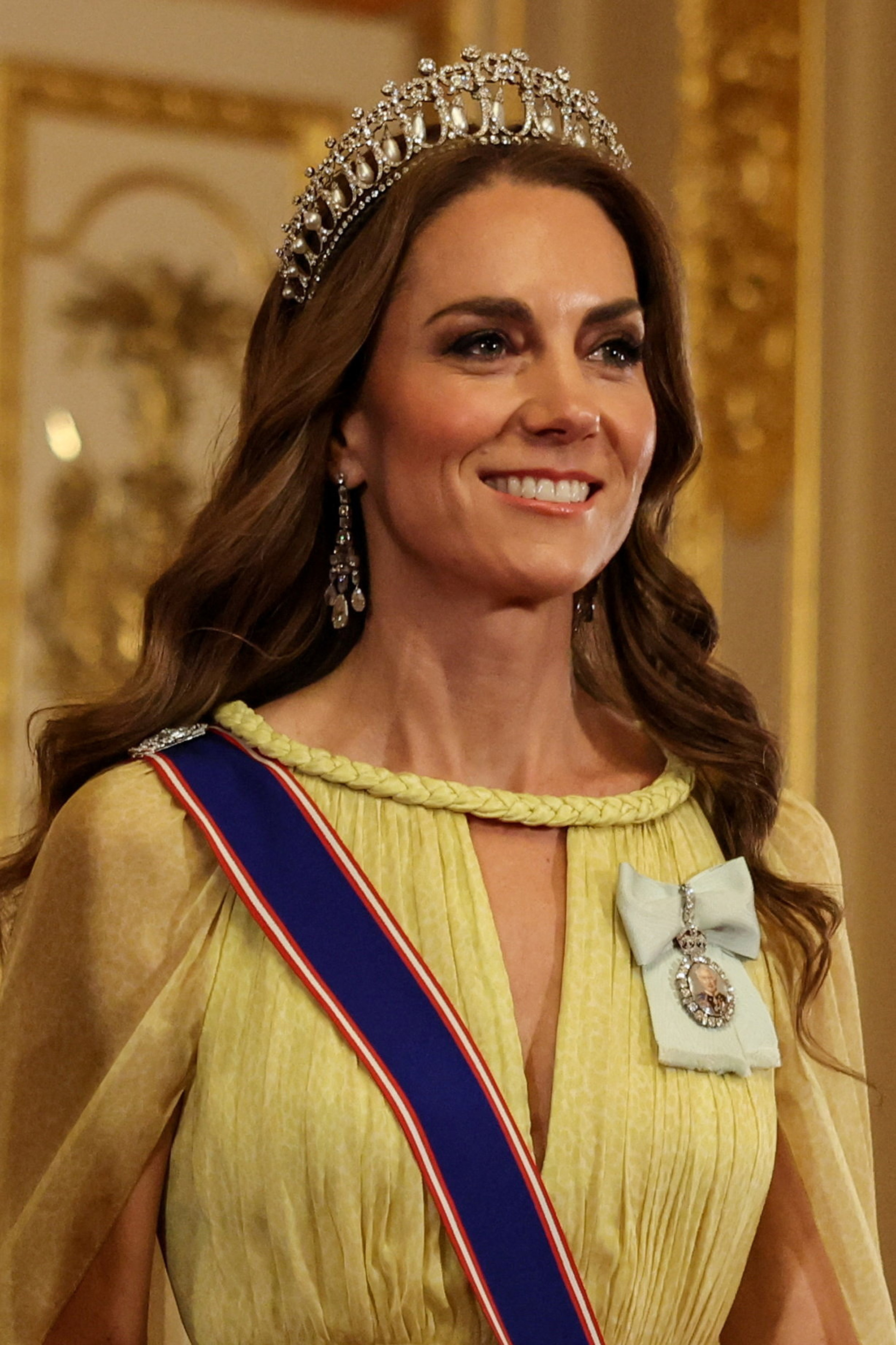 Eine detaillierte Nahaufnahme zeigt Catherine, Prinzessin von Wales, wie sie die prächtigen königlichen Juwelen präsentiert, die sie bei den Abendfeierlichkeiten am 20. Oktober 2026 trug. Auf ihrem locker gewellten Haar thront Königin Marys „Lover’s Knot“-Tiara, ergänzt durch Königin Elizabeth II.s Perlen-Ohrringe, während die Porträtminiatur von König Charles III. aus dem Royal Family Order elegant auf einer hellblauen Seidenschleife neben dem geflochtenen Kragen des Kleides ruht. | Quelle: Getty Images