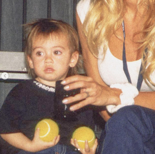 Auf einer intimen Retro-Aufnahme sitzt der junge Dylan Jagger Lee und hält zwei gelbe Tennisbälle fest, während seine Mutter Pamela Anderson, die ein weißes Tanktop und eine blaue Hose trägt, liebevoll ihren Arm neben ihn legt. Als sie während der Feiertage über ihren Weg als Mutter nachdachte, feierte sie das tiefe Fundament der Liebe, das ihr Leben prägt: „Die Liebe … und der Stolz, den ich empfinde – als Mutter der süßesten Brandon und Dylan … Ohne sie wäre meine Liebesgeschichte nicht vollständig. 🤍“ | Quelle: Instagram/pamelaanderson