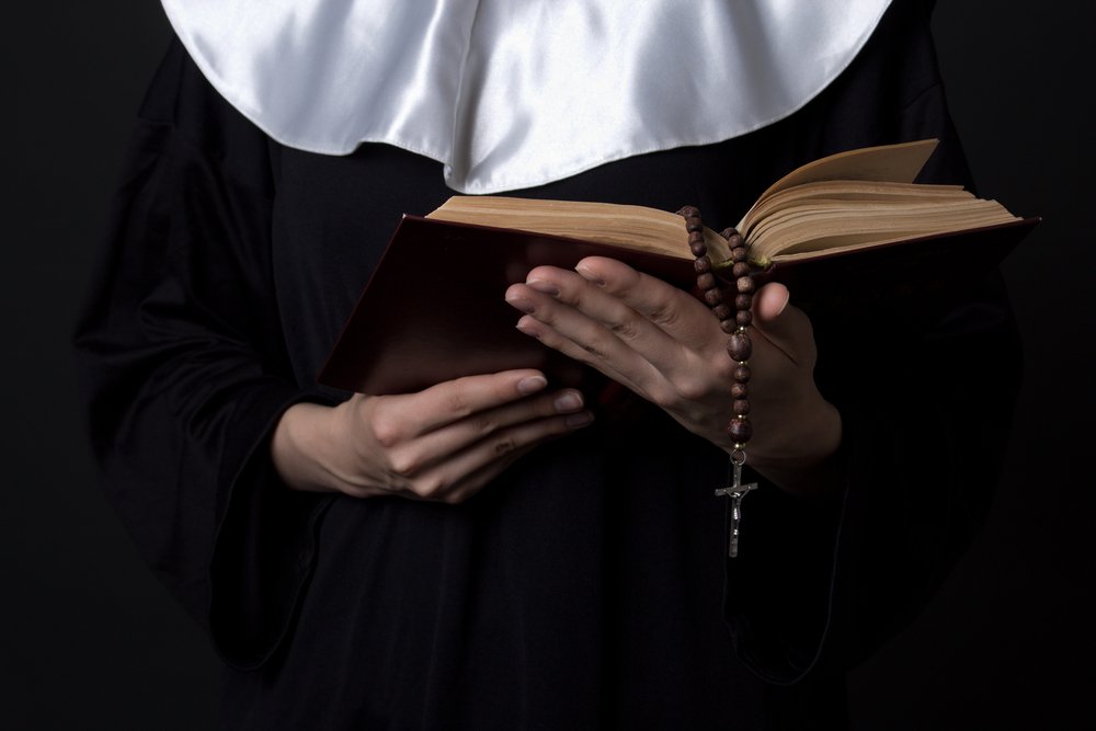 Eine Nonne in Kutte hält ein Buch. | Quelle: Shutterstock