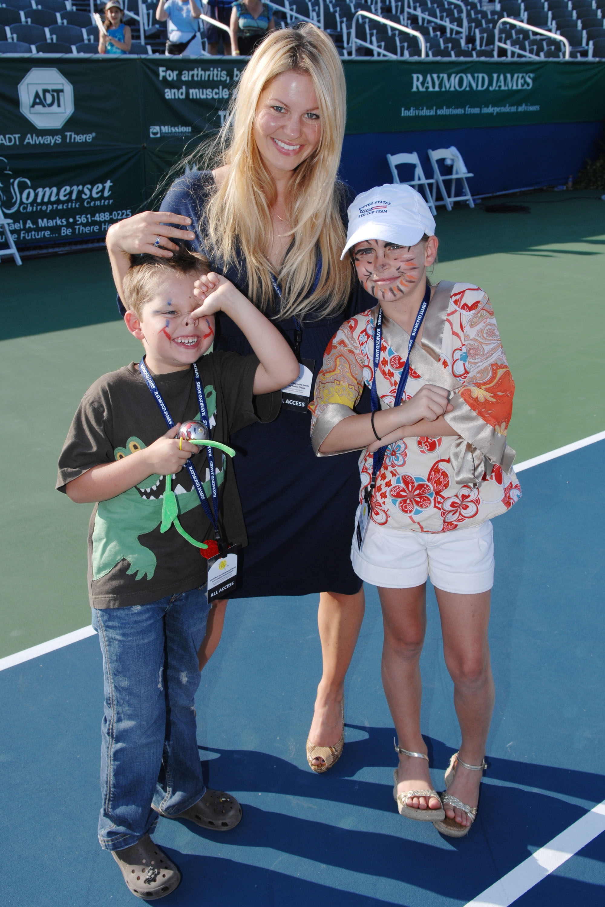 Candace Cameron Bure posiert auf dem Platz mit ihren Kindern, Tochter Natasha Bure und ihrem jüngeren Sohn Maksim Bure, während des Chris Evert/Raymond James Pro-Celebrity Tennis Classic im Delray Beach Tennis Center am 4. November 2007 in Delray Beach, Florida. Die stolze Mutter lächelt in einem marineblauen Kleid und Peep-Toe-Pumps neben ihren Kindern mit bemalten Gesichtern – der kleine Maksim trägt ein T-Shirt mit Dinosaurier-Motiv und Jeans, während Natasha eine bunte Bluse mit Blumenmuster, weiße Shorts und eine Baseballkappe trägt. | Quelle: Getty Images