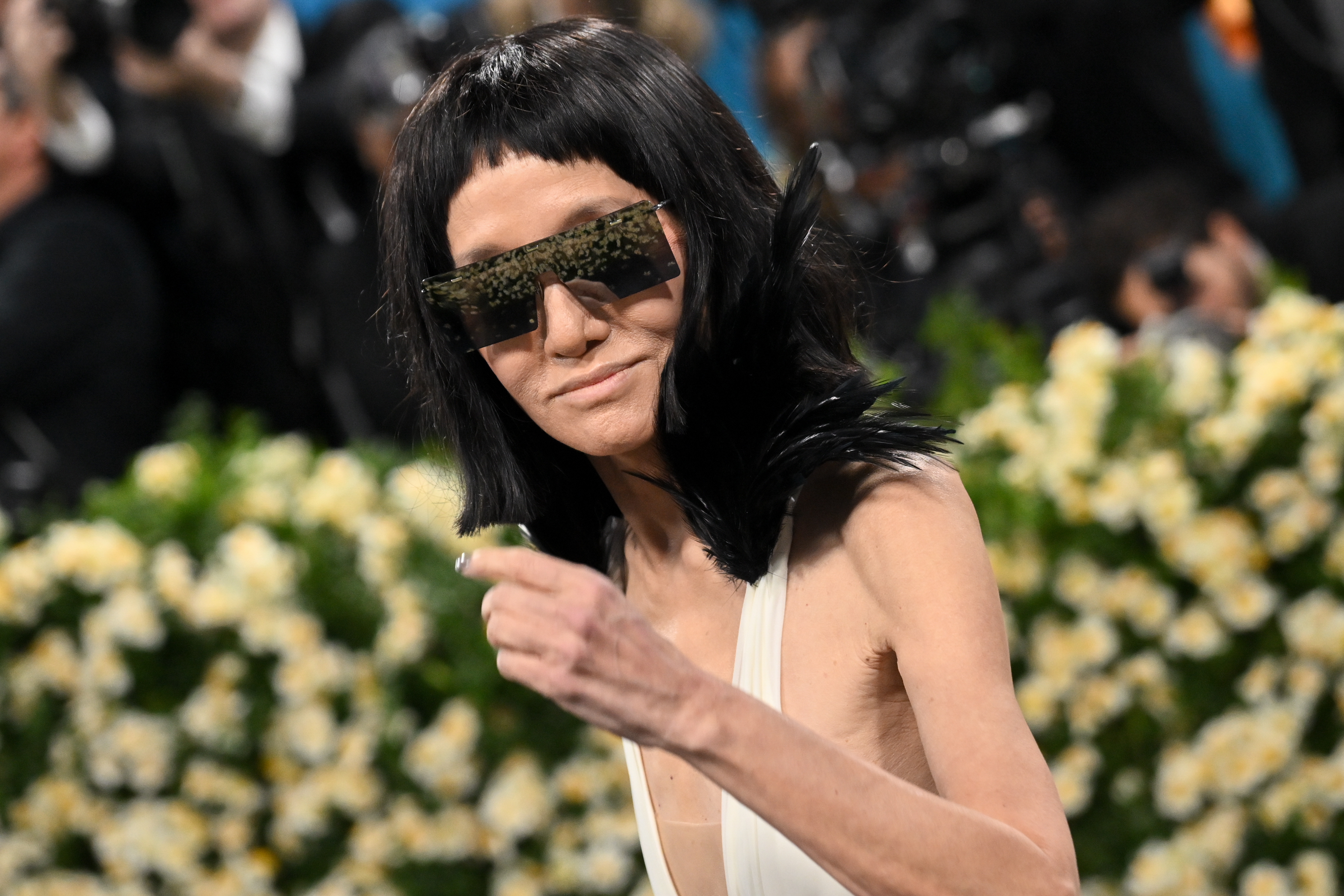 In einem freimütigen Moment gestikuliert Vera Wang in die Menge, während ihre verspiegelte Sonnenbrille und ihr gefiedertes Dekolleté die Energie des Abends widerspiegeln.