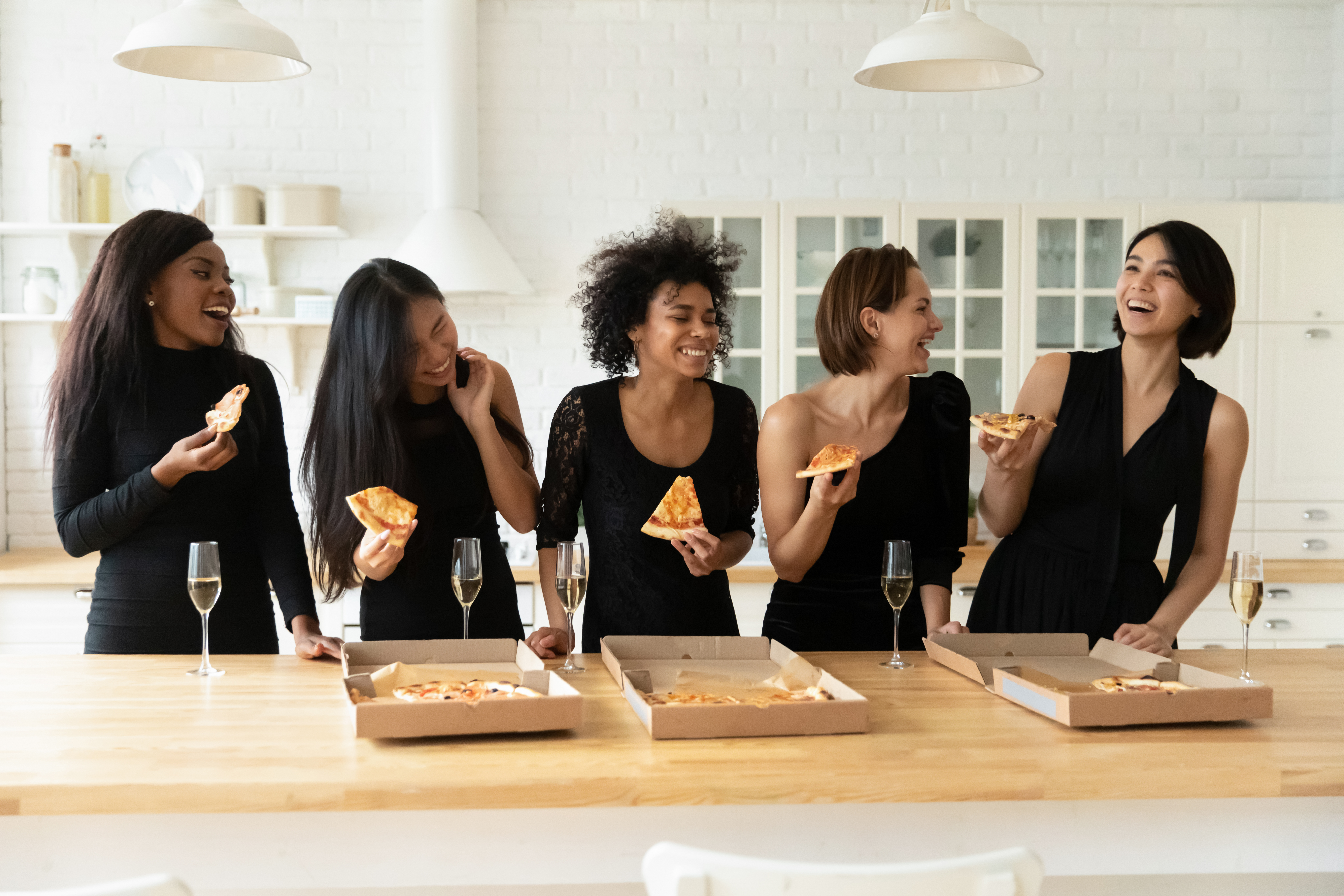 Schwarz gekleidete Frauen essen Pizza und trinken Champagner | Quelle: Shutterstock
