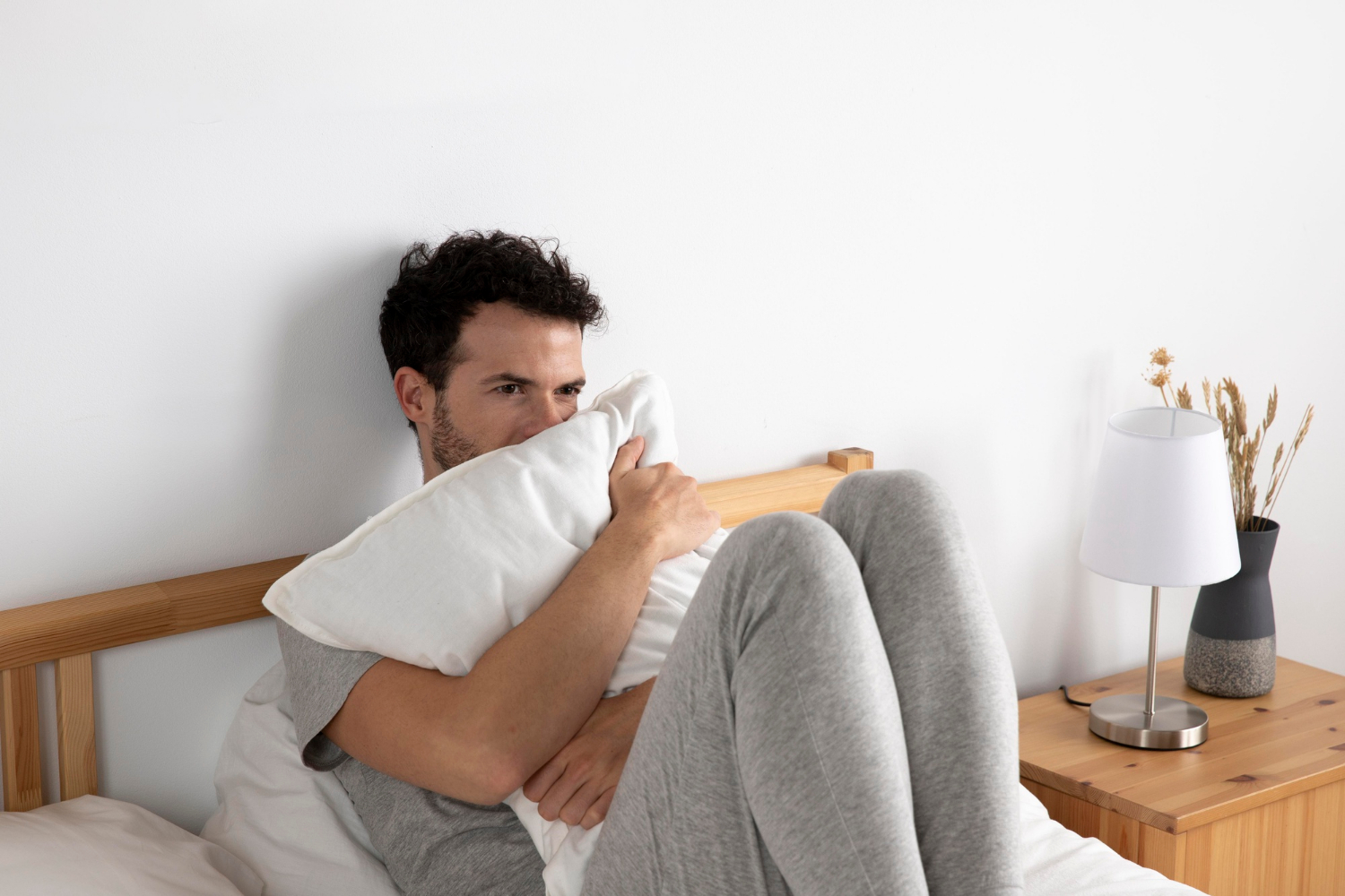Ein ängstlicher Mann, der ein Kissen hält und auf dem Bett sitzt | Quelle: Freepik