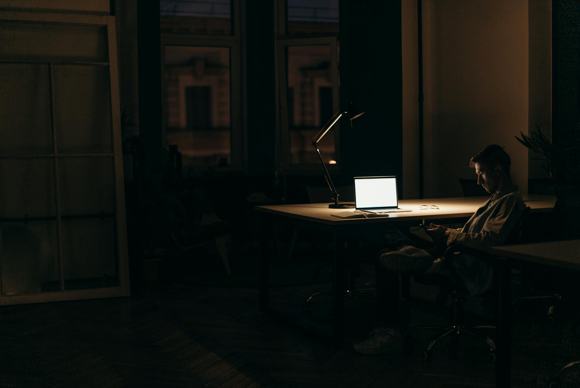 Ein Mann sitzt an einem Schreibtisch in einem dunklen Raum | Quelle: Pexels