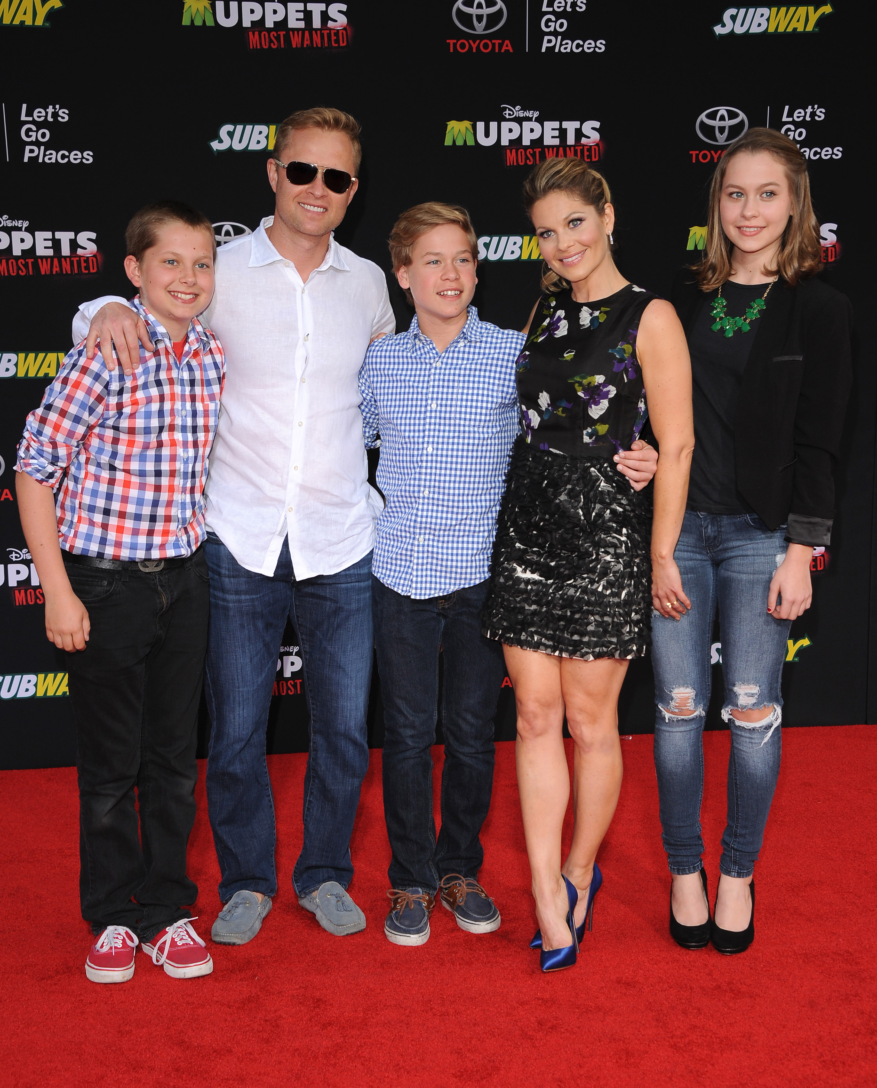 Candace Cameron Bure erscheint zusammen mit ihrem Ehemann Valeri Bure und ihren Kindern – Lev, Maksim und Natasha – bei der Premiere von „Muppets Most Wanted“ im El Capitan Theatre am 11. März 2014 in Hollywood, Kalifornien. Die Schauspielerin sieht umwerfend aus in einem gemusterten, ärmellosen Minikleid und leuchtend blauen Satin-Pumps, flankiert von Tochter Natasha in Used-Jeans und einem schwarzen Blazer, während ihr jüngster Sohn Maksim in der Mitte strahlt – er trägt ein blaues Gingham-Hemd mit Knöpfen und dunkle Jeans. | Quelle: Getty Images