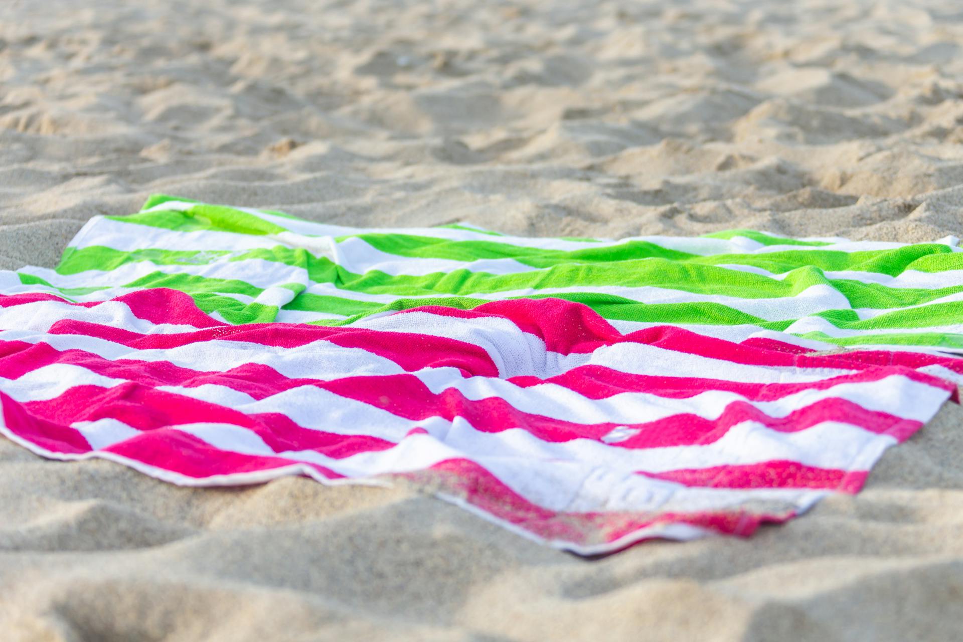 Leuchtend rosa und grün gestreifte Handtücher auf dem Sand | Quelle: Pexels