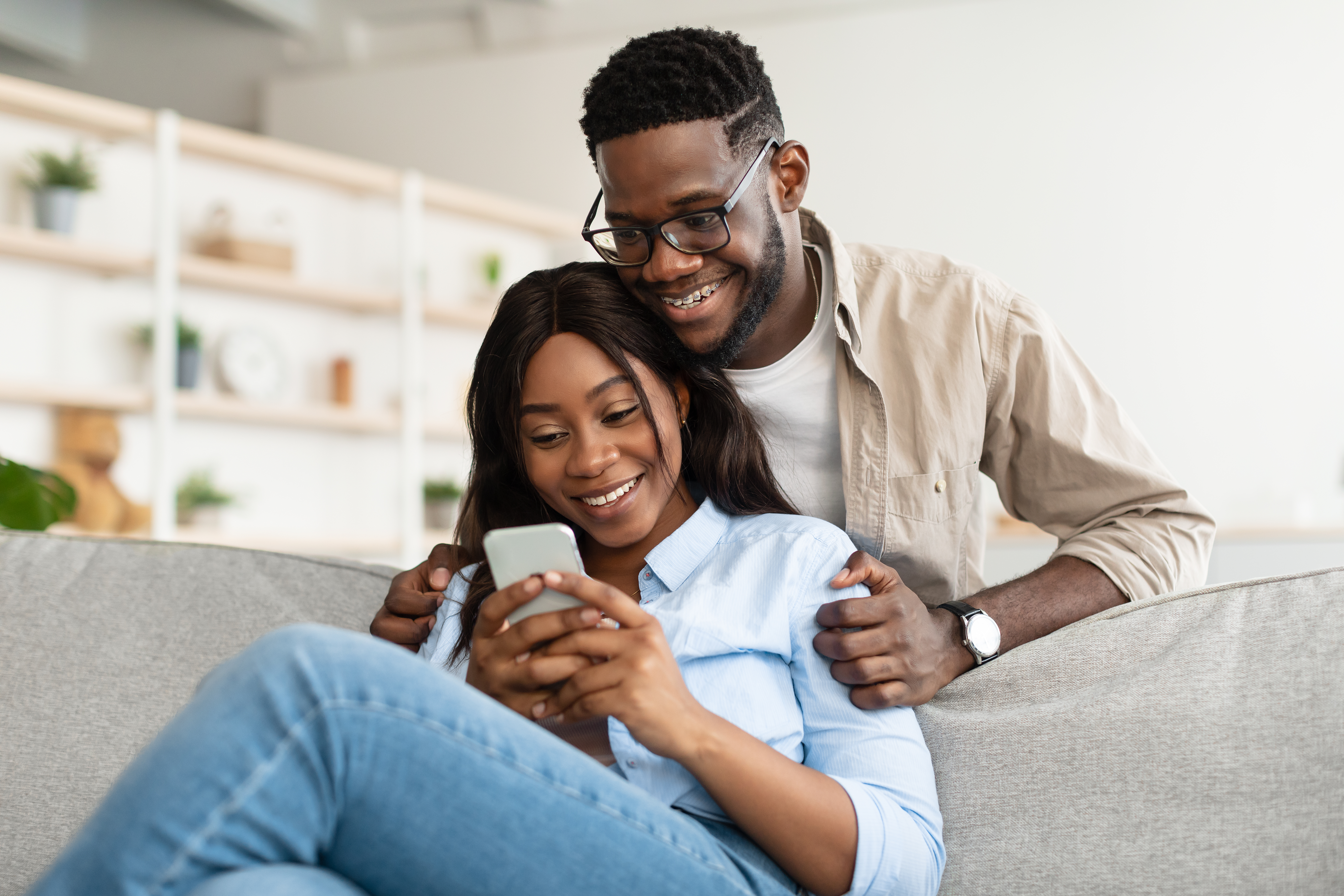Ein afroamerikanisches Paar sitzt auf der Couch und benutzt ein Mobiltelefon | Quelle: Getty Images