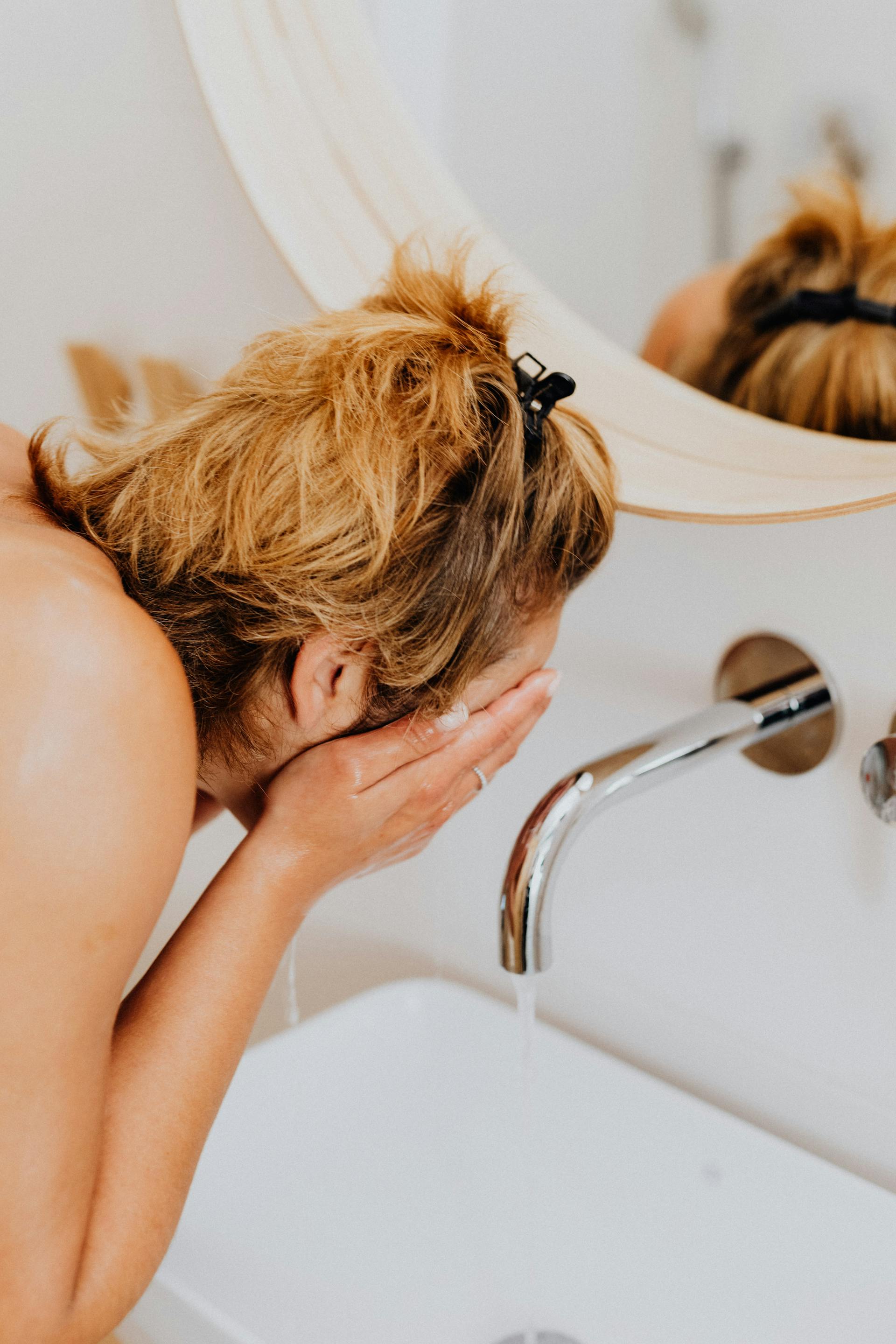 Eine Frau, die sich im Waschraum Wasser ins Gesicht spritzt | Quelle: Pexels