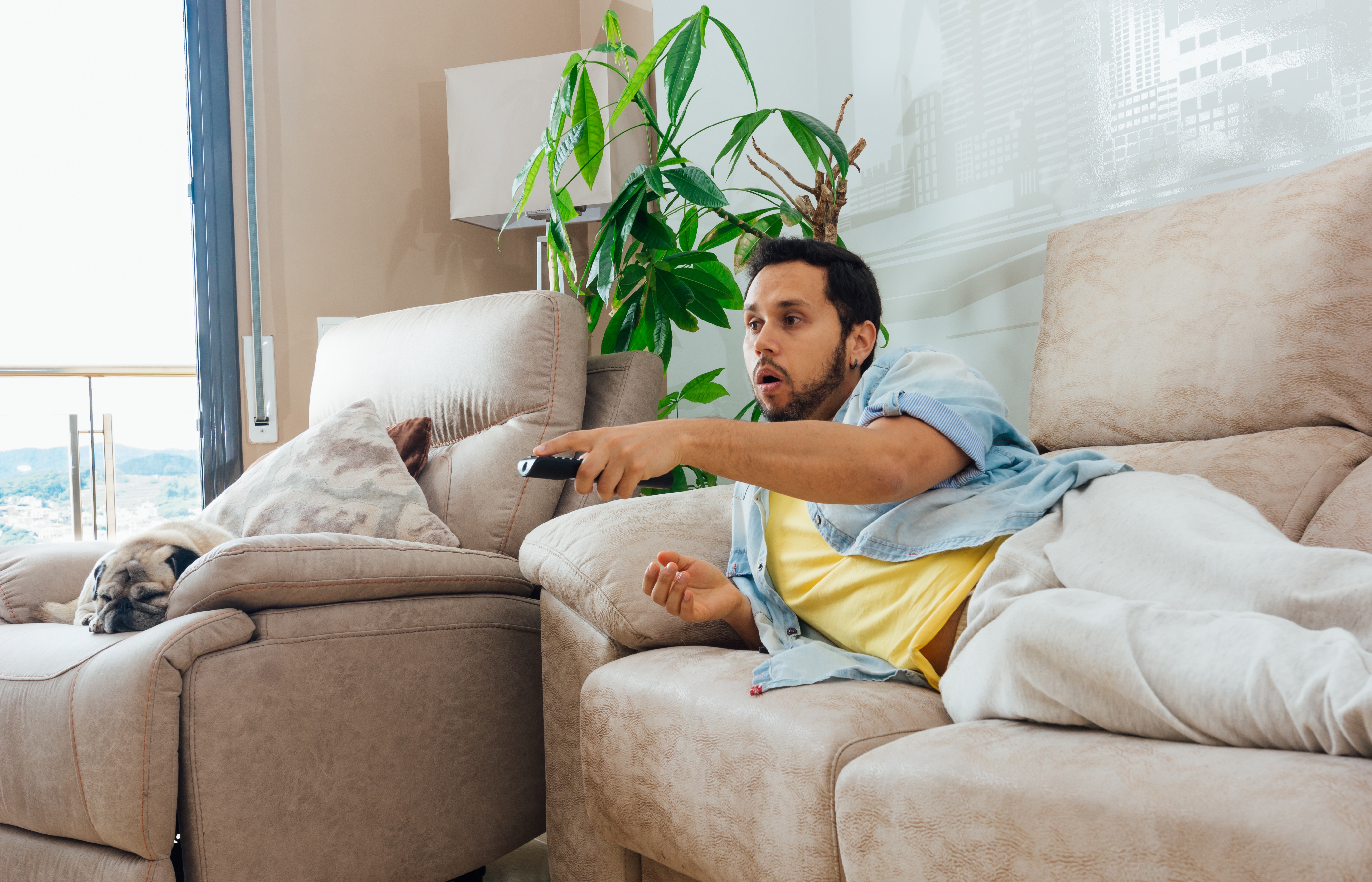 Mann auf einer Couch mit der TV-Fernbedienung | Quelle: wirestock auf Freepik