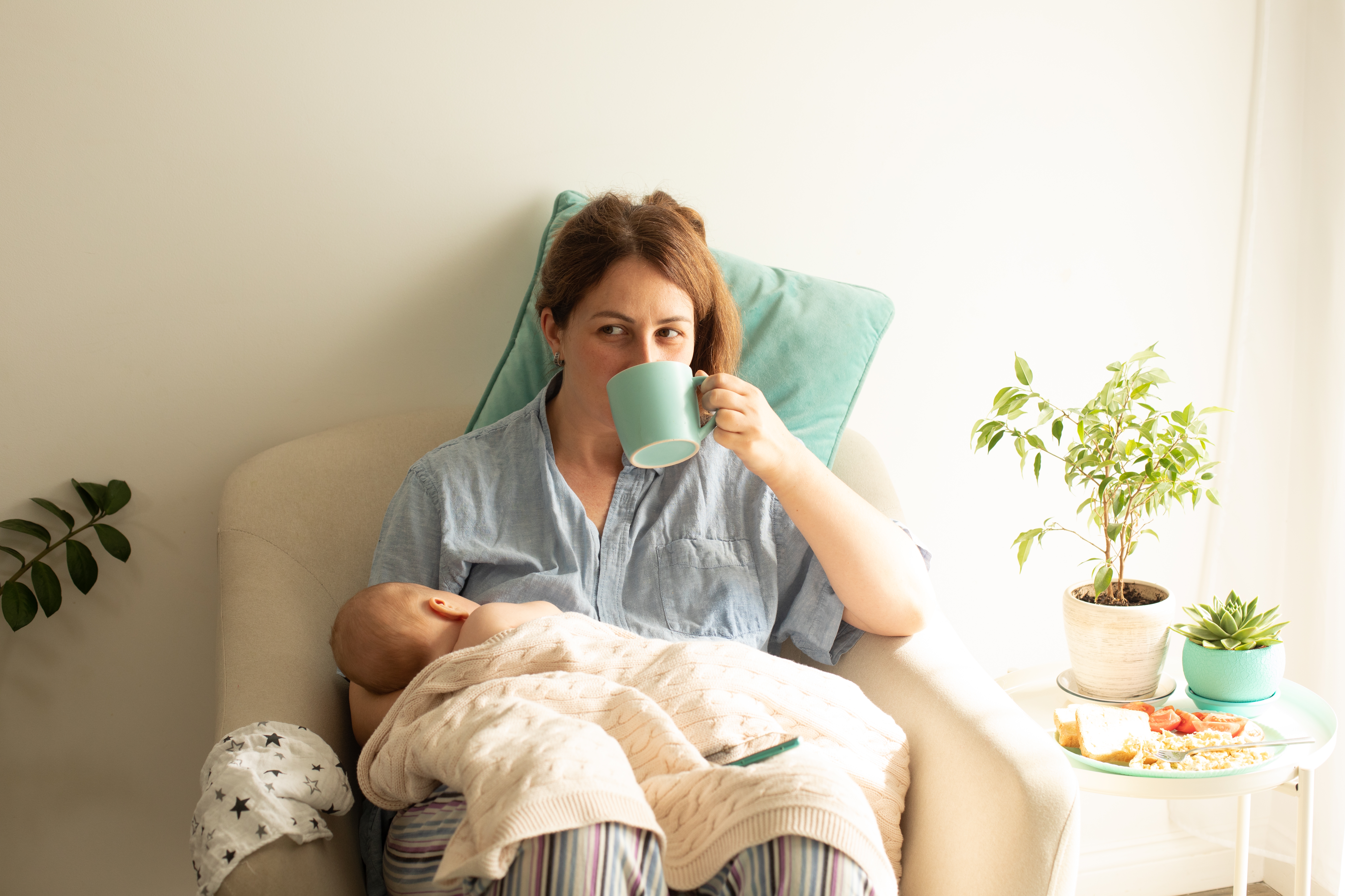 Eine Frau, die ihr Neugeborenes stillt, während sie Tee trinkt | Quelle: Shutterstock