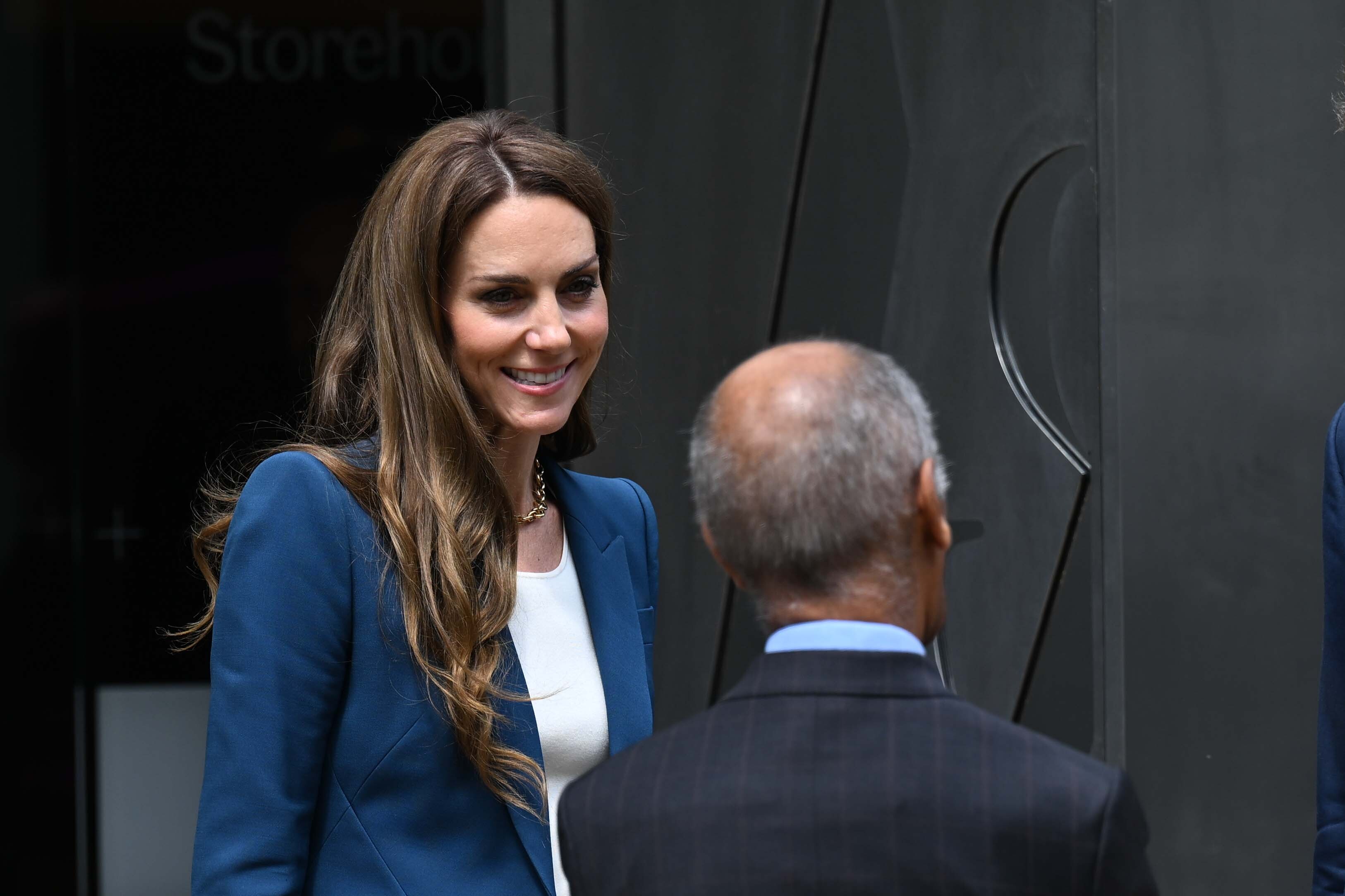 Prinzessin Catherine zeigt ein subtiles Lächeln, während sie aufmerksam zuhört und ihren Kopf in einer aktiven, aufnahmebereiten Haltung leicht neigt. Ihr strahlender Gesichtsausdruck und ihr sanfter Blick verleihen diesem Moment eine nachdenkliche Note.