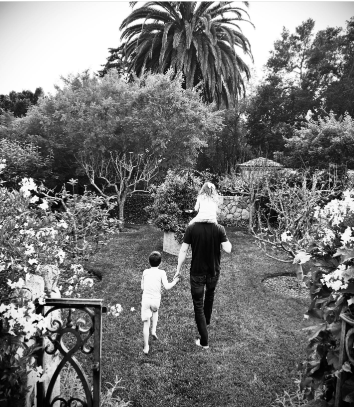 Prinz Harry spaziert mit seinen Kindern durch einen gepflegten Garten, trägt Prinzessin Lilibet auf den Schultern und hält dabei Prinz Archies Hand. | Quelle: Instagram/meghan