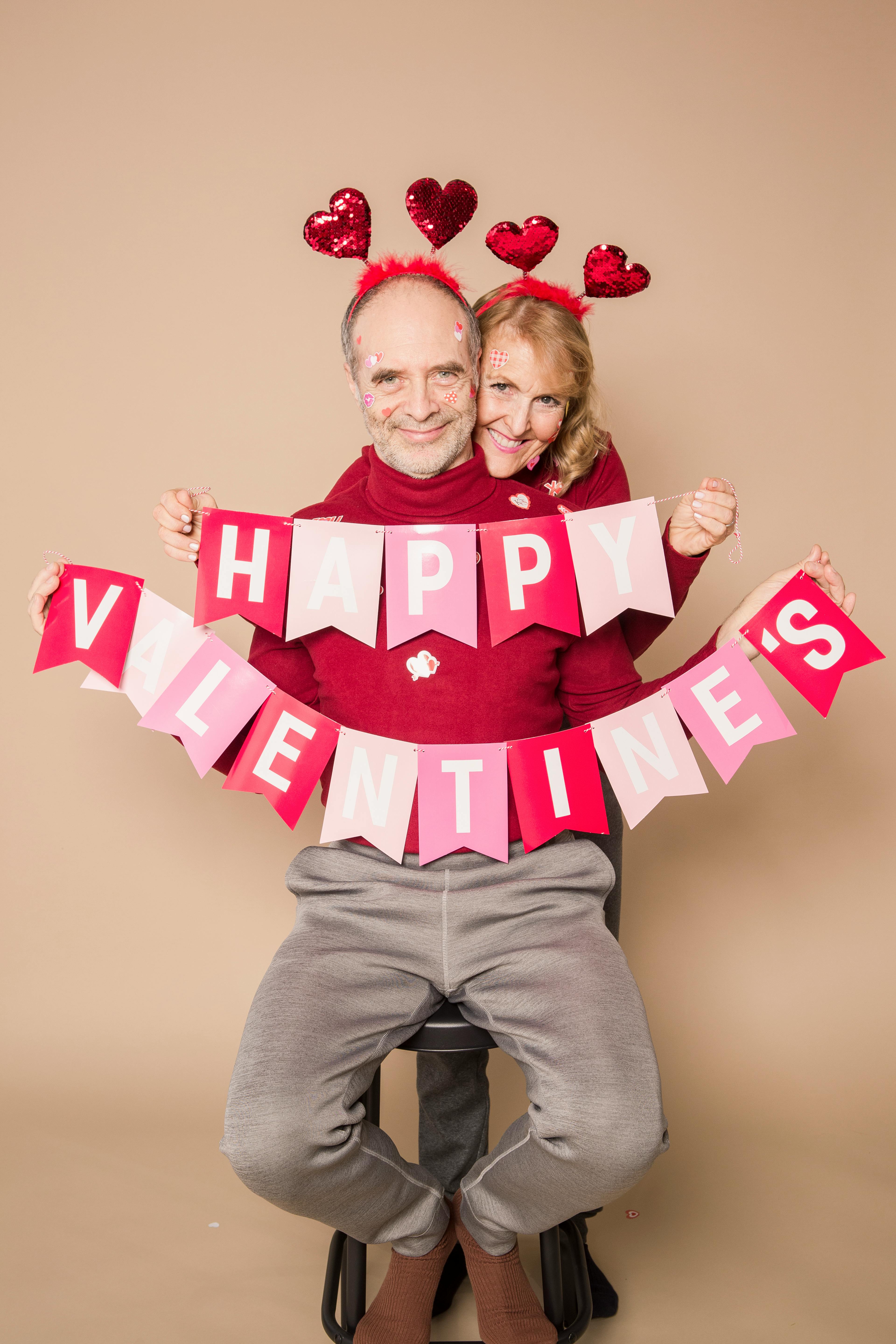 Ein Paar in passenden Outfits hält eine hängende Dekoration mit der Aufschrift "Happy Valentine’s." | Quelle: Pexels