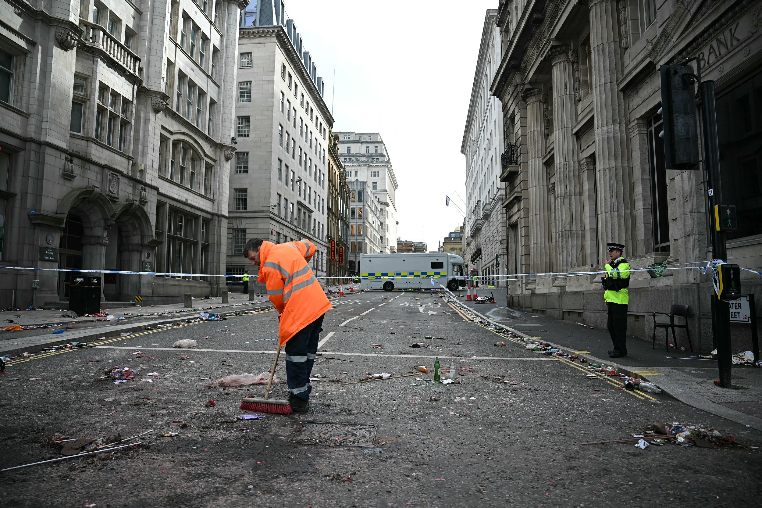 Ein Arbeiter säubert Trümmer, während ein Polizist am 27. Mai 2025 an einer Absperrung in der Water Street in Liverpool, Nordwestengland, steht, nachdem ein Auto in die Menschenmenge gerast ist, die am 26. Mai die Trophäenparade der Premier League in Liverpool verfolgte | Quelle: Getty Images