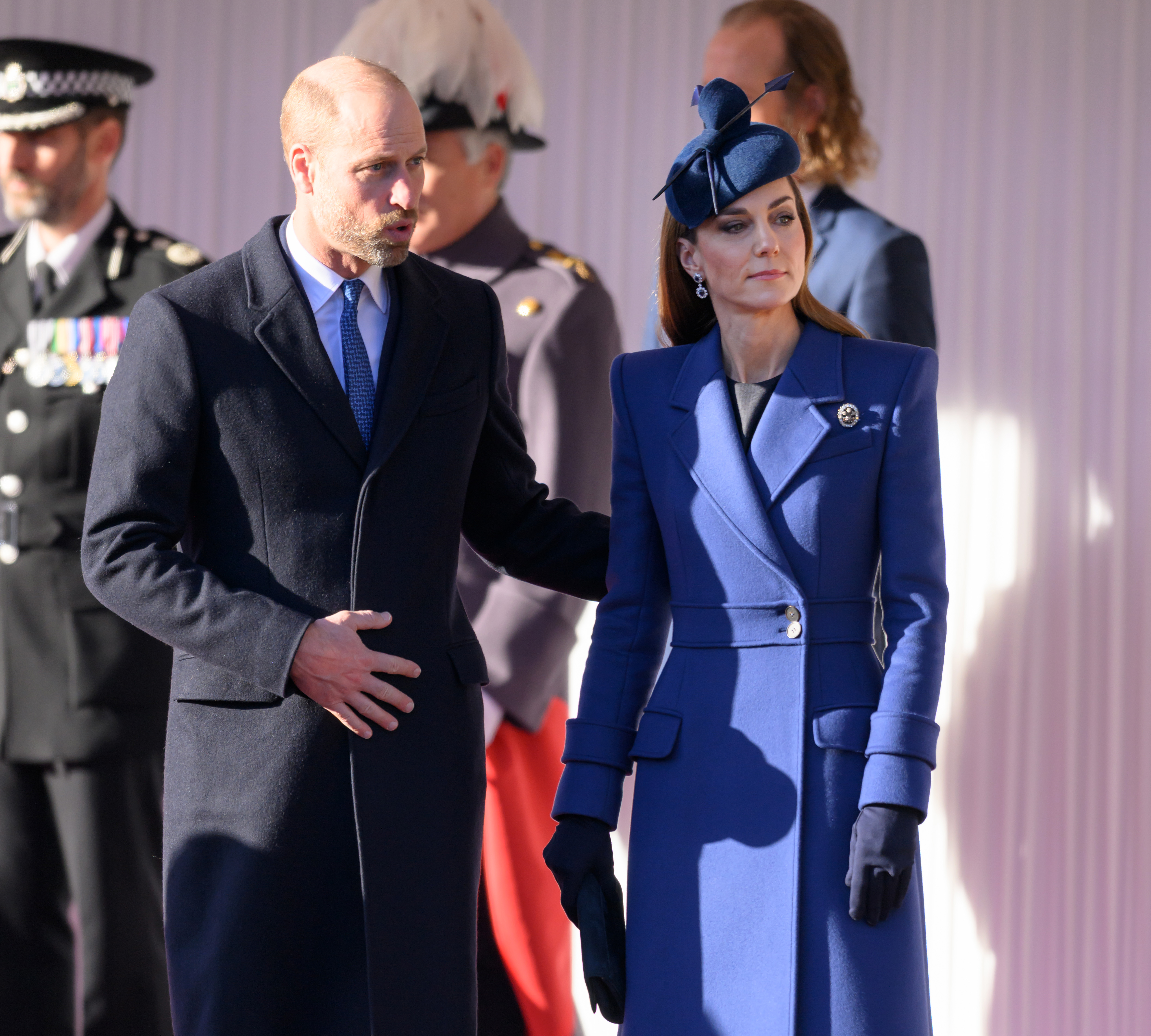 Prinz William und Catherine, Prinzessin von Wales, stehen gemeinsam bei der feierlichen Begrüßung im Windsor Castle am 3. Dezember 2025, die den Beginn des deutschen Staatsbesuchs markiert. Catherine sieht in einem auffälligen kobaltblauen Mantelkleid mit strukturierten Schultern, fallendem Revers und einem Gürtel an der Taille maßgeschneidert und elegant aus. Dazu trägt sie einen passenden, kunstvoll geformten Fascinator mit Schleife, dunkelblaue Handschuhe und eine historische Diamantbrosche. Sie steht neben William, der einen dunklen Mantel und eine blaue Krawatte trägt. | Quelle: Getty Images