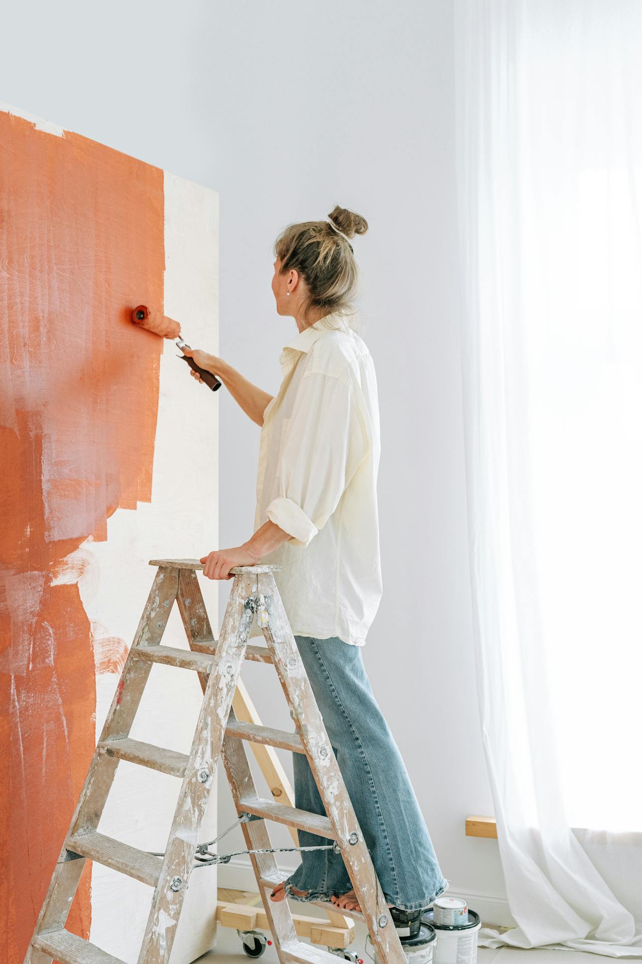 Eine Frau steht auf einer Leiter und streicht eine Wand | Quelle: Pexels