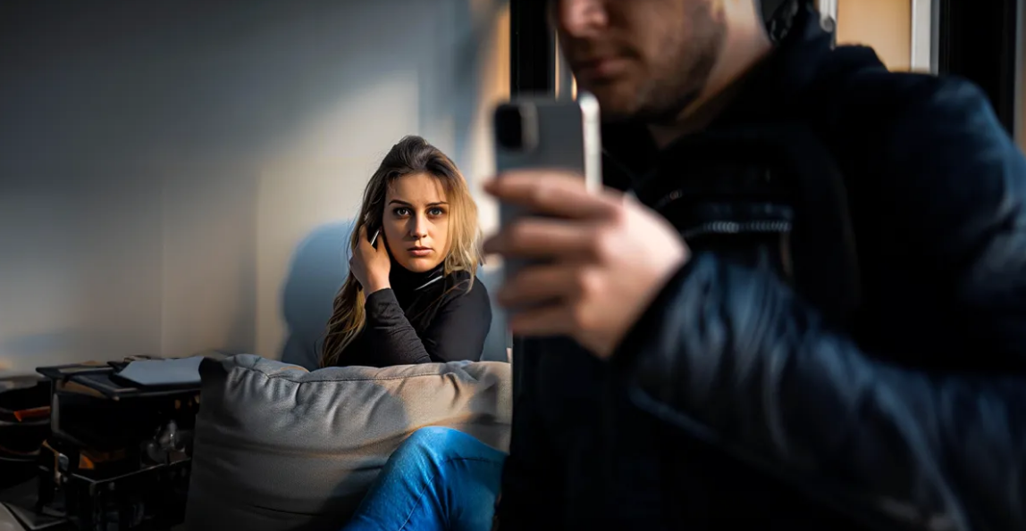 Frau spioniert hinter einem Mann mit einem Telefon her | Quelle: Shutterstock