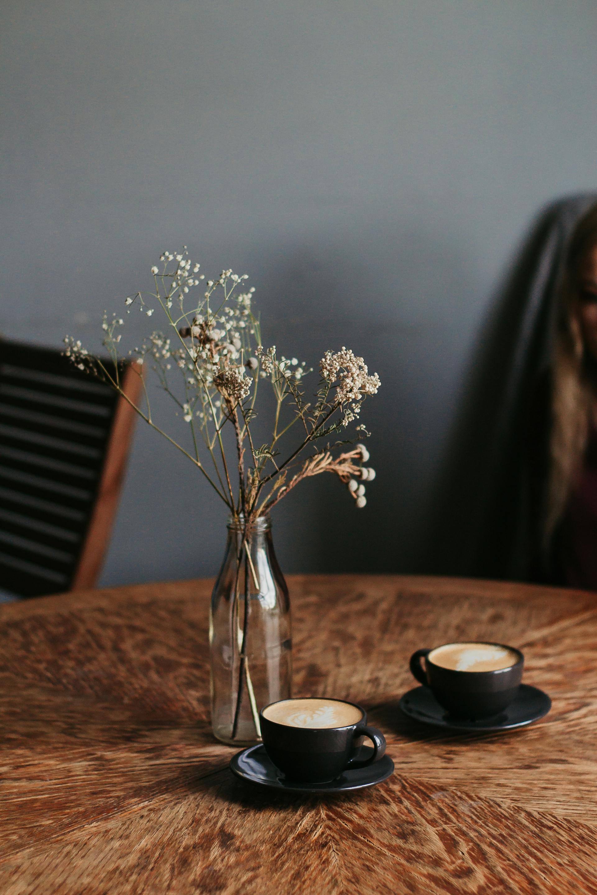 Zwei Tassen Kaffee neben einer Blumenvase auf einem Tisch | Quelle: Pexels