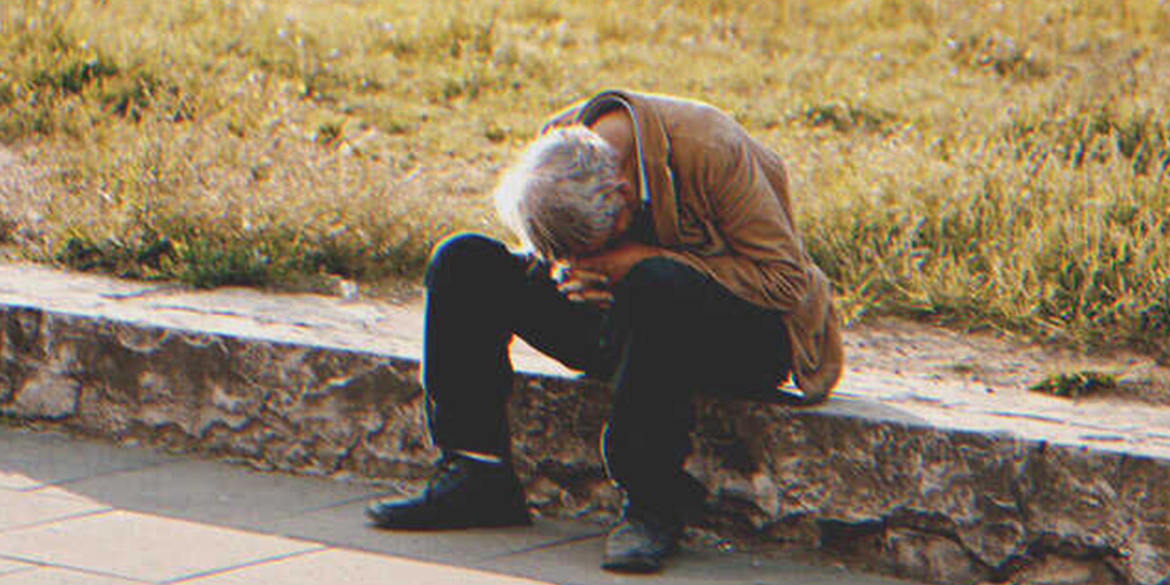 Ein obdachloser Mann sitzt auf dem Gehweg | Quelle: Shutterstock.com