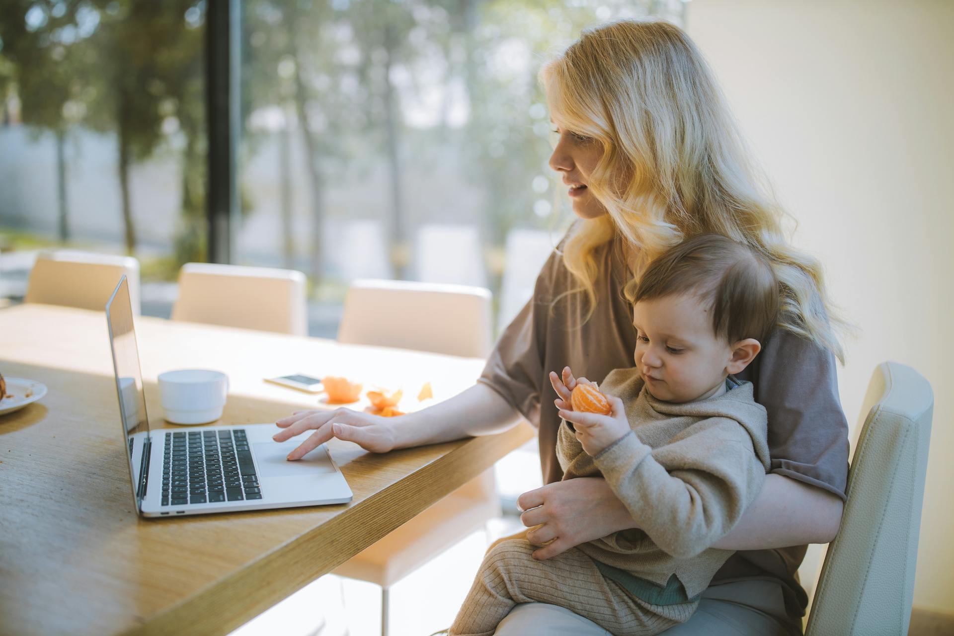 Eine Frau trägt ihren Sohn, während sie einen Laptop benutzt | Quelle: Pexels