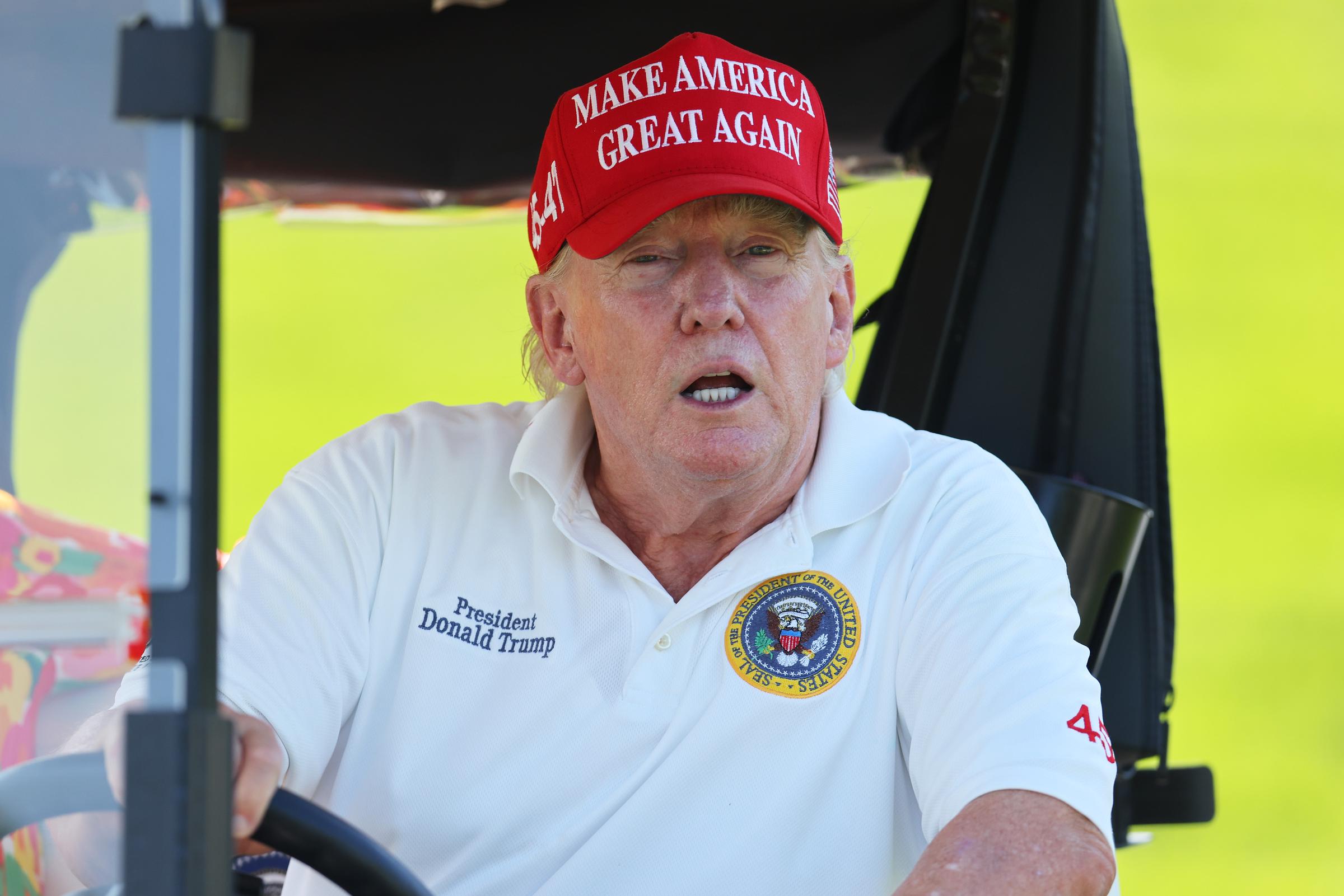 Bei der Veranstaltung in Bedminster in New Jersey am 11. August sitzt Donald Trump in einem Golfwagen und trägt ein weißes Polo mit dem Emblem des Präsidenten. Sein Gesicht wirkt röter als sein Hals, besonders im hellen Außenlicht.