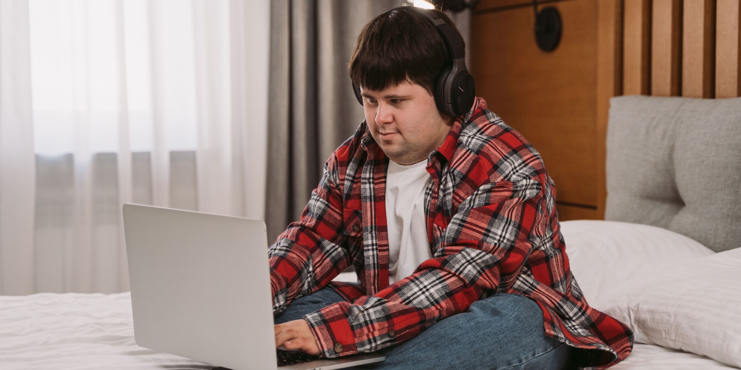 Ein Junge, der Kopfhörer trägt, während er auf einem Bett sitzt und einen Laptop benutzt | Quelle: Pexels