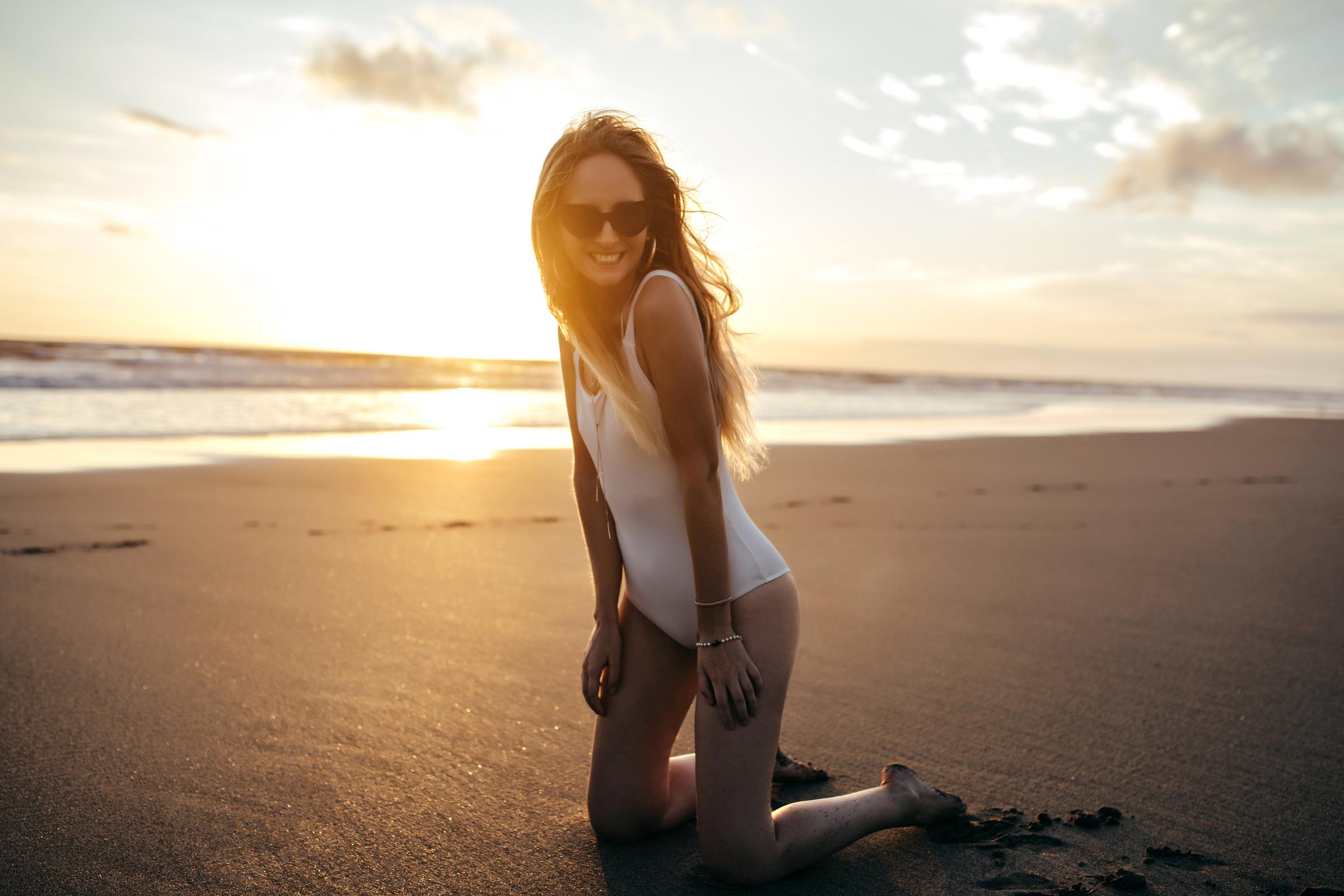 Eine Frau in einem weißen Badeanzug, die am Strand kniet | Quelle: Freepik