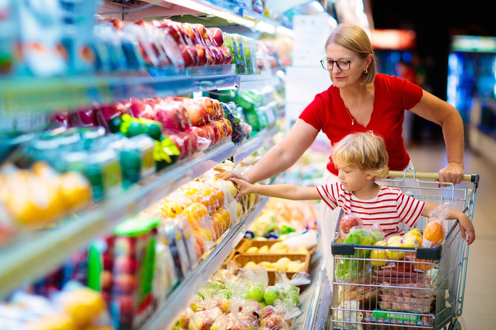Eine Frau mit einem Kind in dem Einkaufswagen in einem Supermarkt. | Quelle: Shutterstock